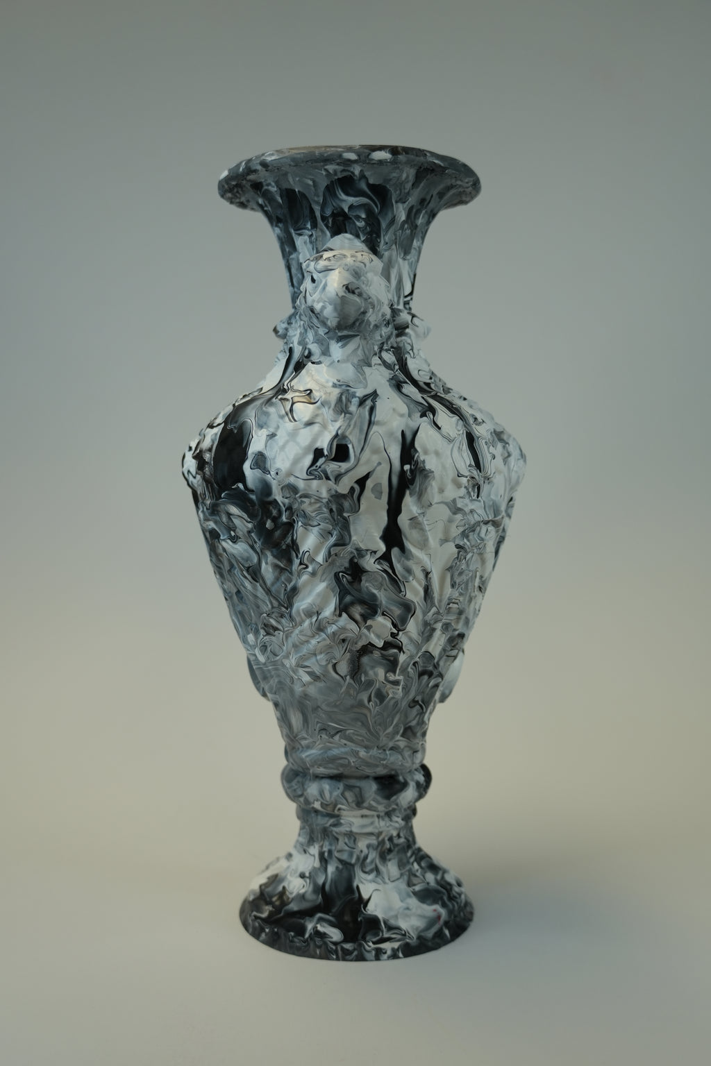 A sculptural vase with a flared rim and pedestal base, featuring an abstract marbled pattern in black, white, and gray, photographed against a neutral gray gradient background.