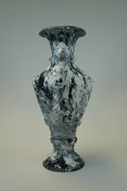 A sculptural vase with a flared rim and pedestal base, featuring an abstract marbled pattern in black, white, and gray, photographed against a neutral gray gradient background.