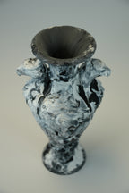 A sculptural vase with a flared rim and two side handles, featuring a marbled black and white textured glaze, photographed against a neutral light gray background.