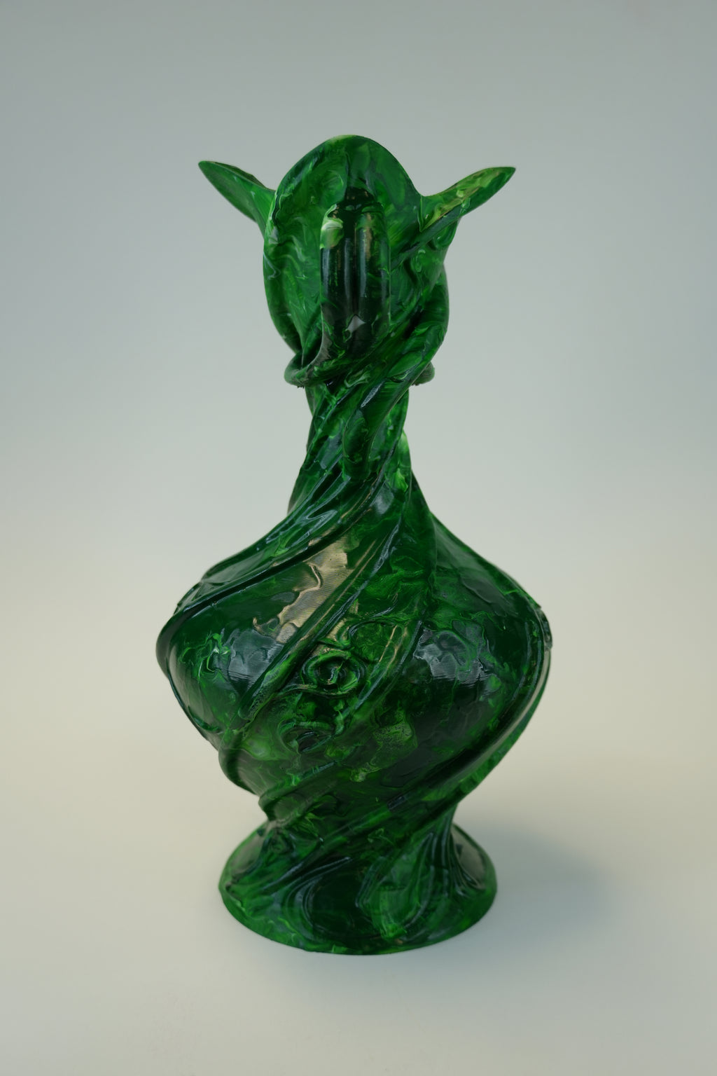 A sculptural green vase with a stylized animal or dragon-like head and curved, twisted body, photographed against a plain light gray studio background.