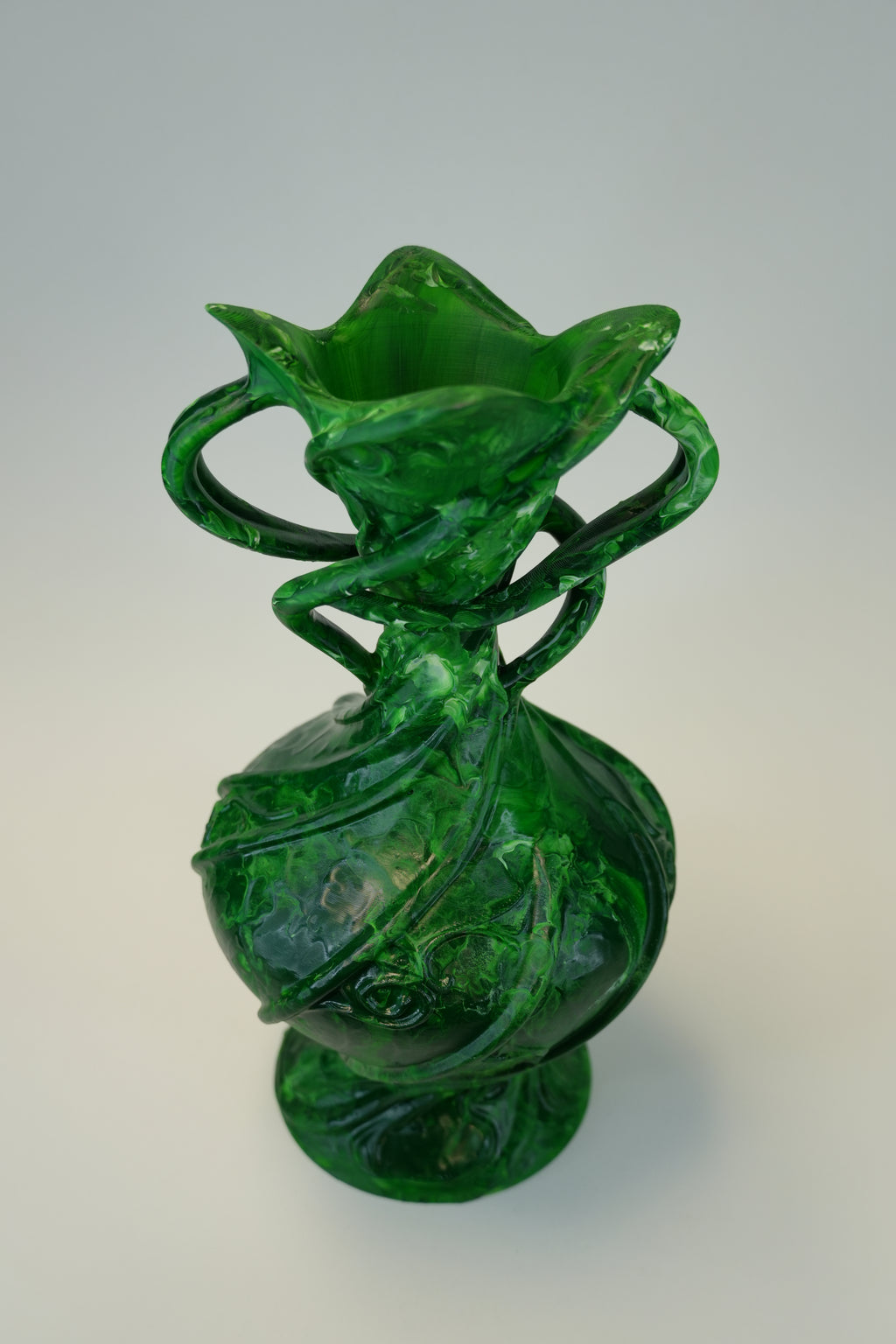 A translucent green glass vase with a flared, multi-lobed rim, two loop handles, and a bulbous body with swirling glass patterns, shown on a neutral light gray background.