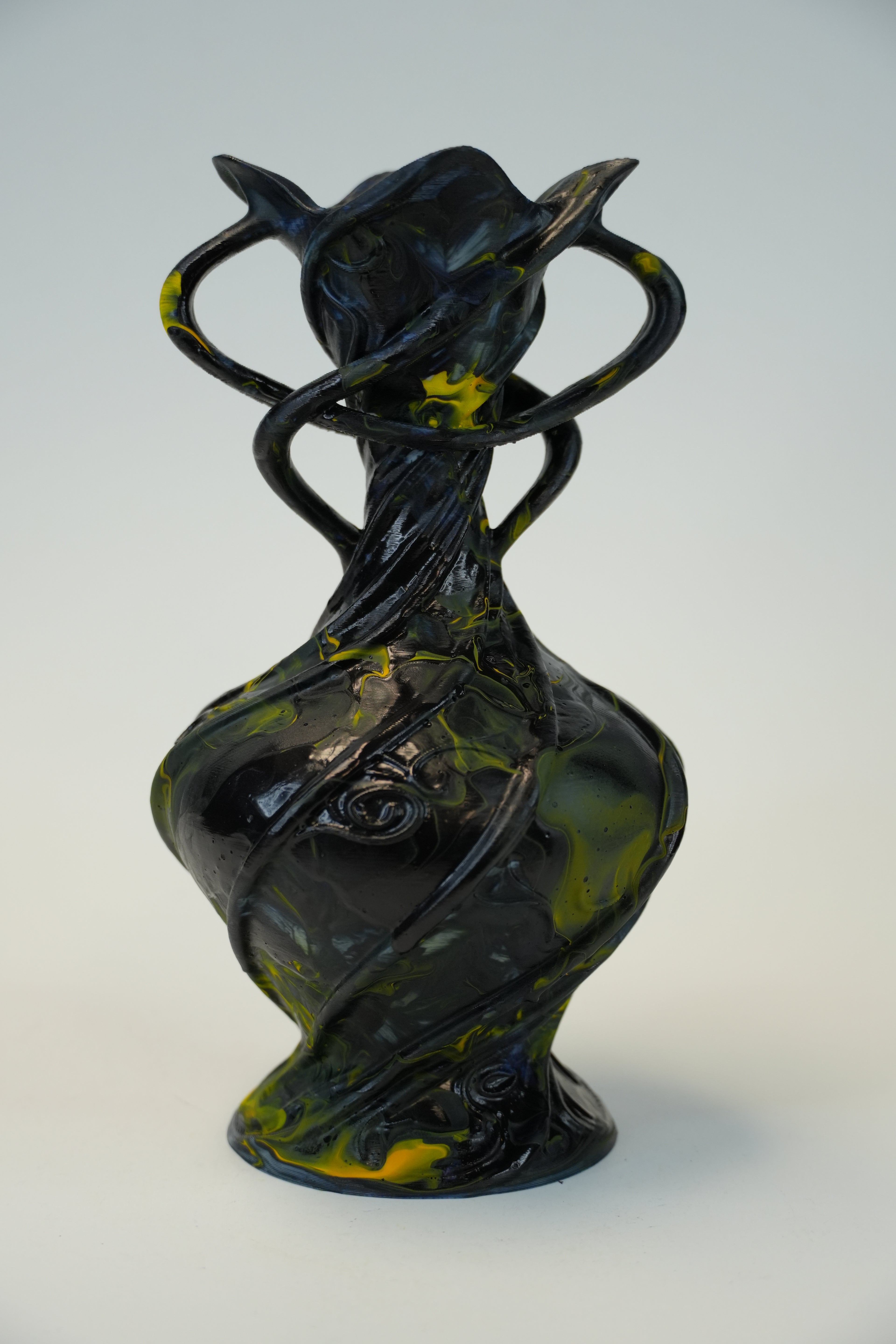 An abstract sculptural vase with a glossy black finish and marbled olive-green and yellow accents, set against a plain light gray background.