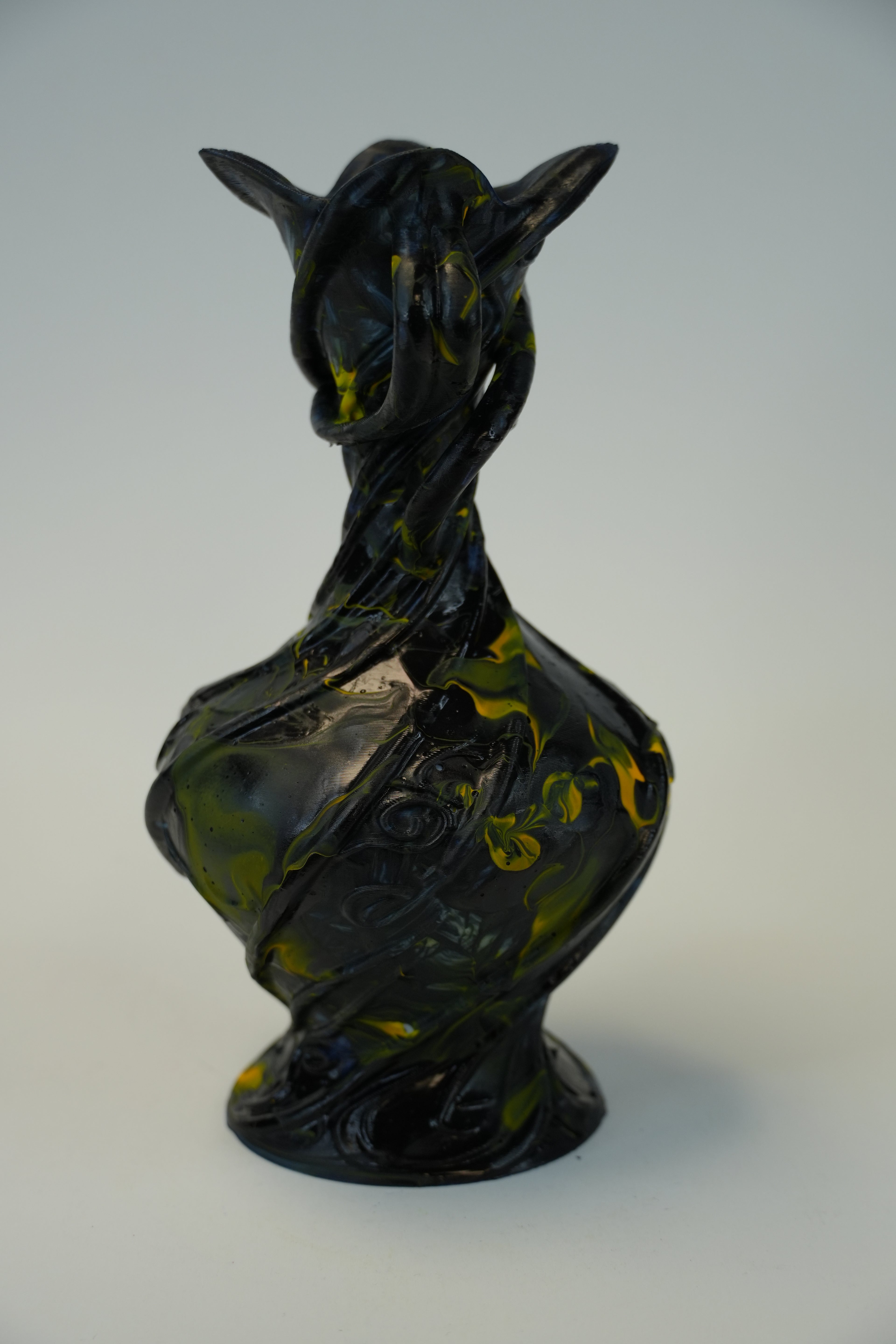 A sculptural glass vase with a stylized animal head design, featuring a glossy black and olive green marbled pattern, set against a neutral light gray background.