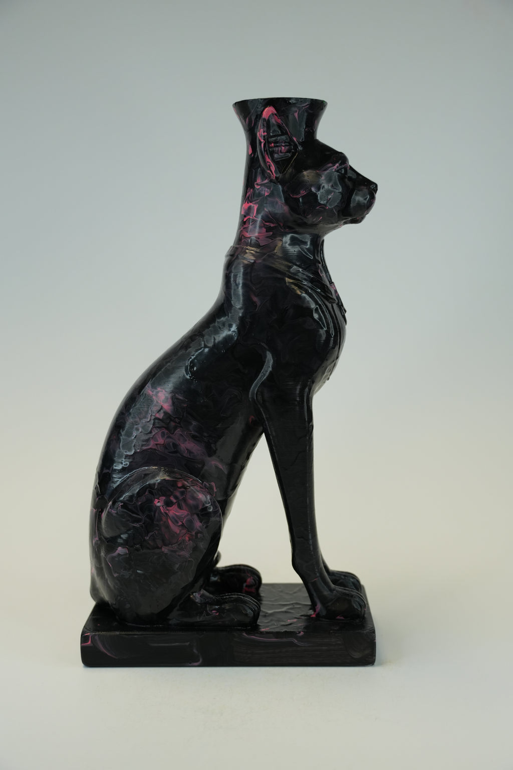 A glossy black cat figurine with pink marbled inclusions, shown in a seated pose on a matching rectangular base against a neutral light gray background.