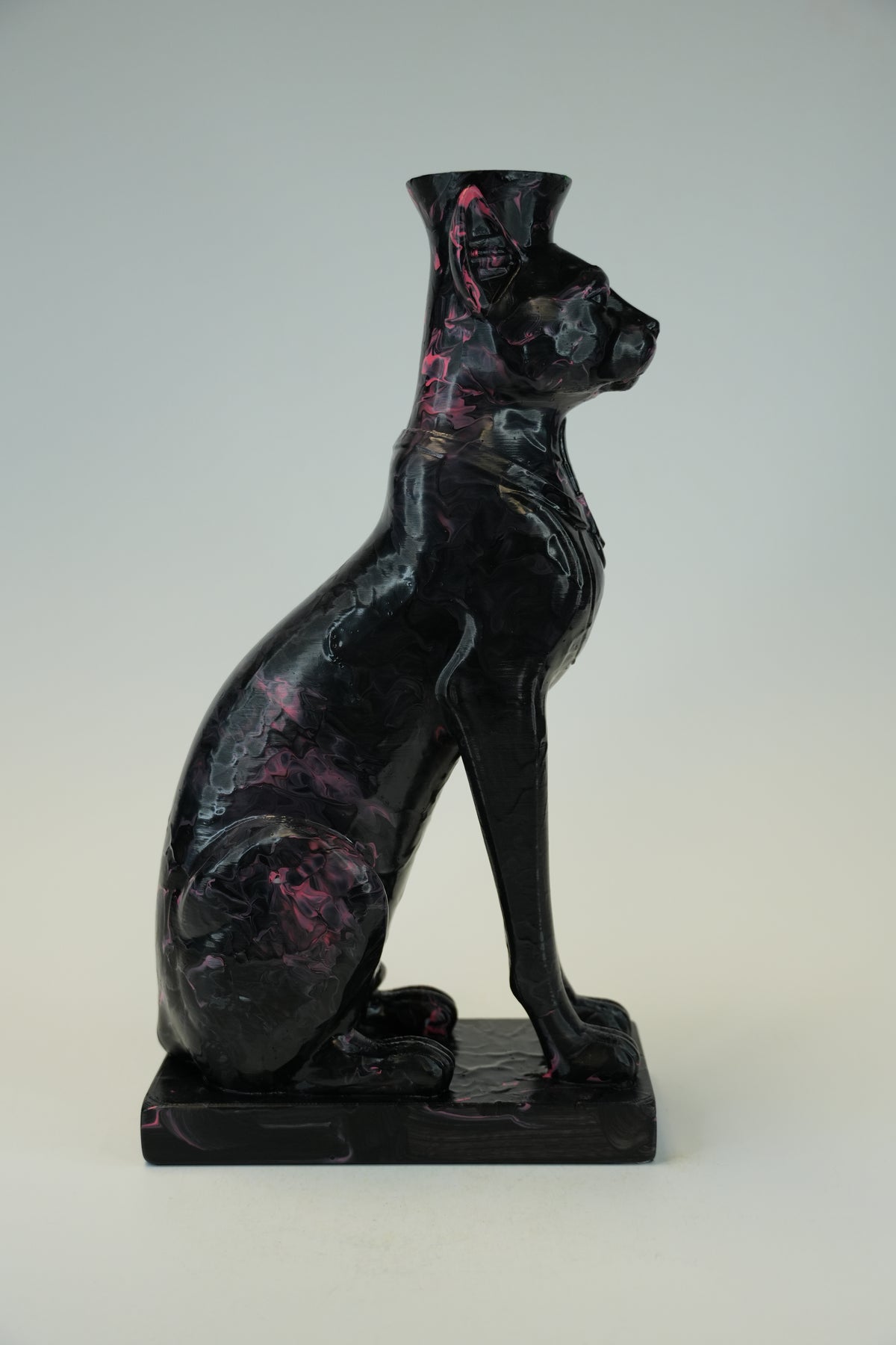 A glossy black cat figurine with pink marbled inclusions, shown in a seated pose on a matching rectangular base against a neutral light gray background.