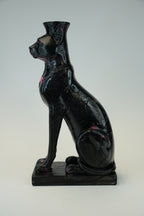 A glossy black cat-shaped vase or sculpture with a flared top, shown in profile on a rectangular base against a light gray studio background.