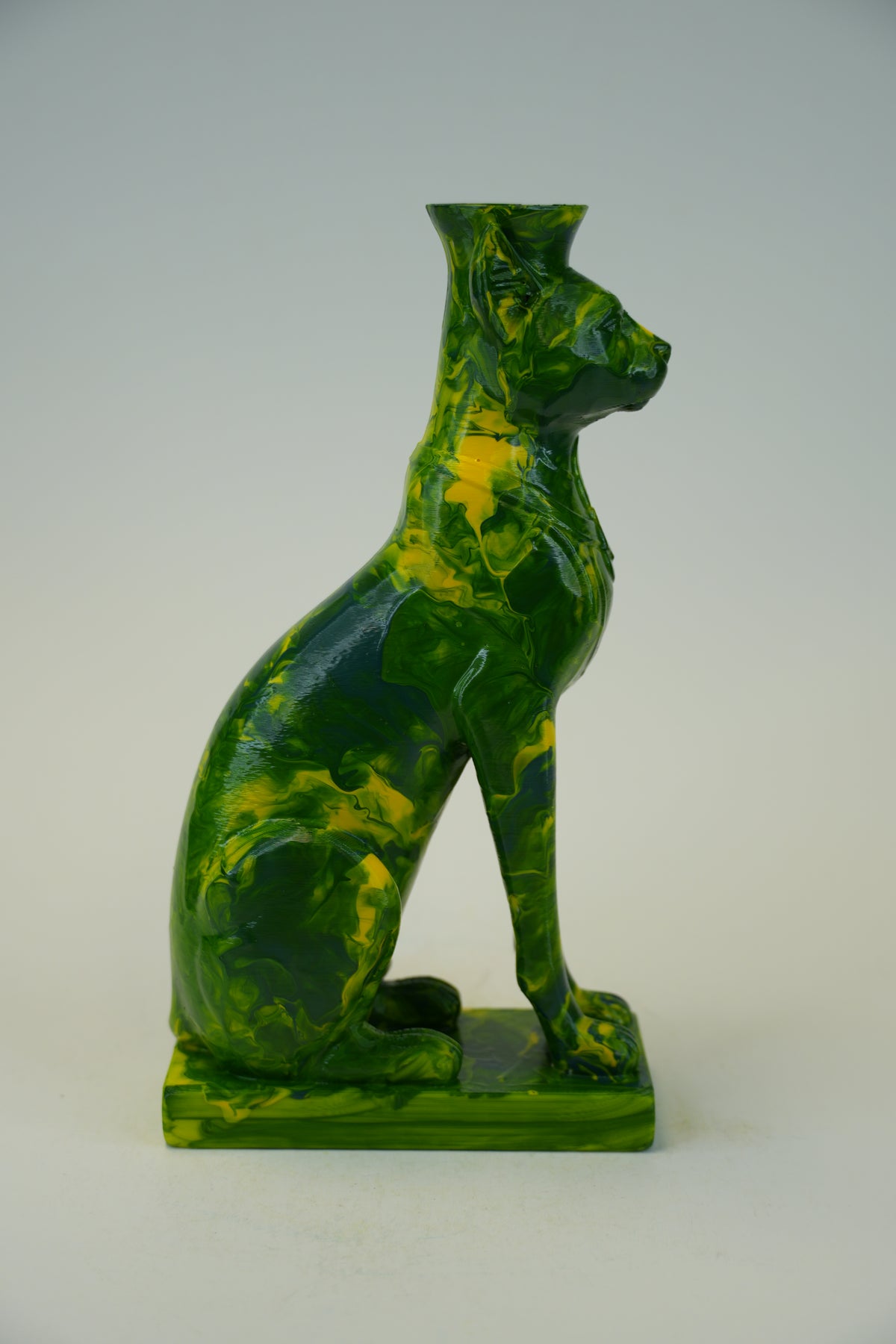 A glossy green and yellow marbled ceramic cat figurine, shaped like a seated cat, on a light gray background.