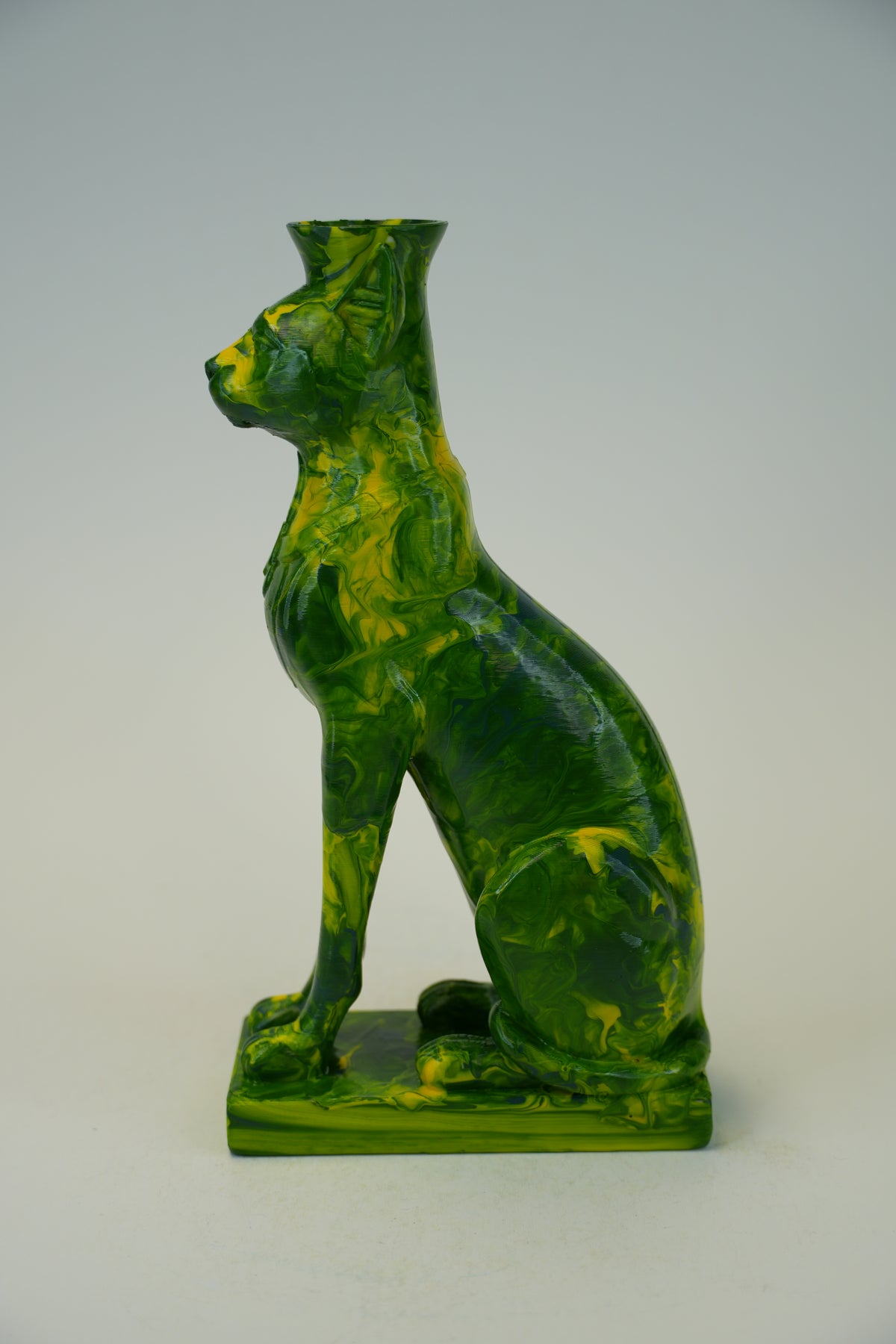 A green and yellow marbled ceramic cat figurine with a tall neck, designed as a vase or candle holder, shown against a neutral light gray background.