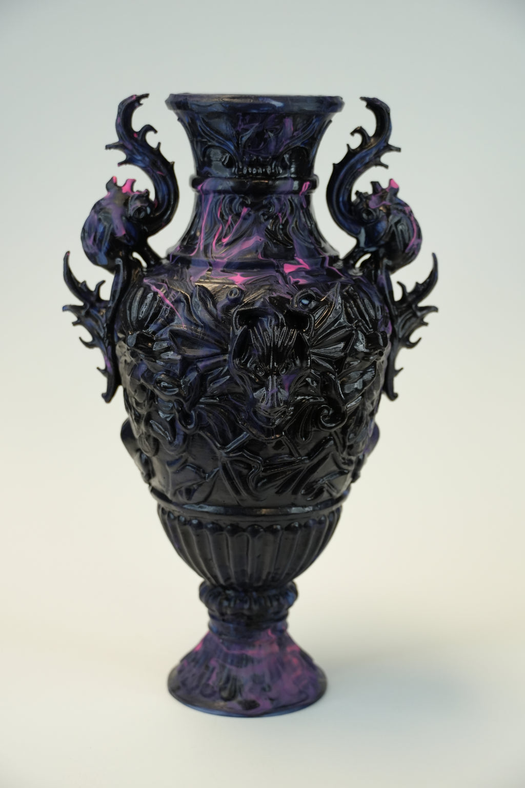 An ornate dark purple and black carved ceramic vase with dragon-like side handles and floral relief details, photographed against a plain light background.