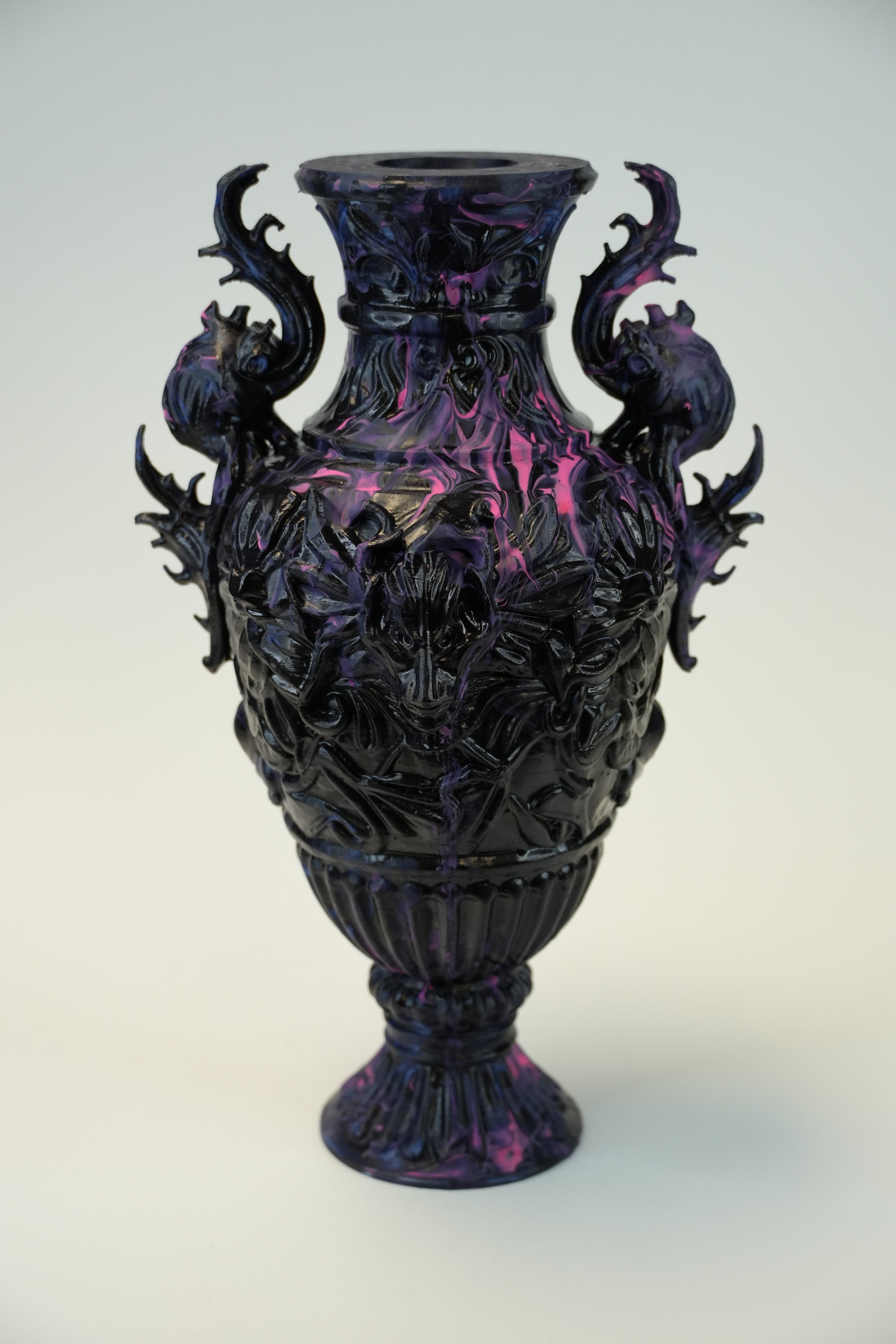 An ornate dark purple and black glass vase with intricate floral relief carvings and two decorative side handles, shown against a plain light background.