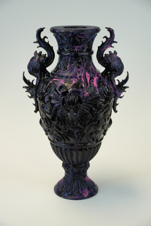 An ornate dark purple and black glass vase with intricate floral relief carvings and two decorative side handles, shown against a plain light background.