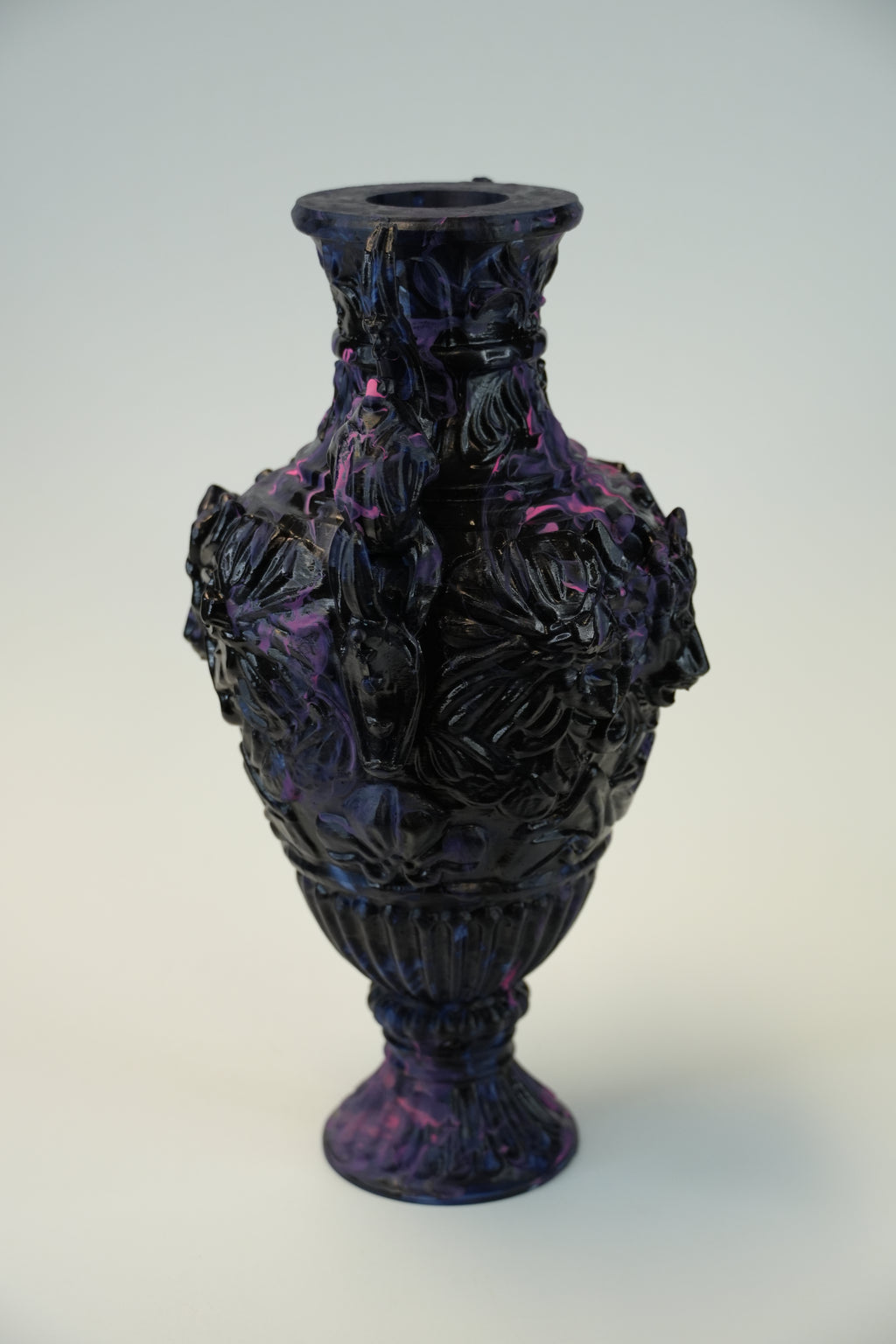 A dark, glossy sculptural vase with a textured, organic surface in black and purple tones, photographed against a plain light background.
