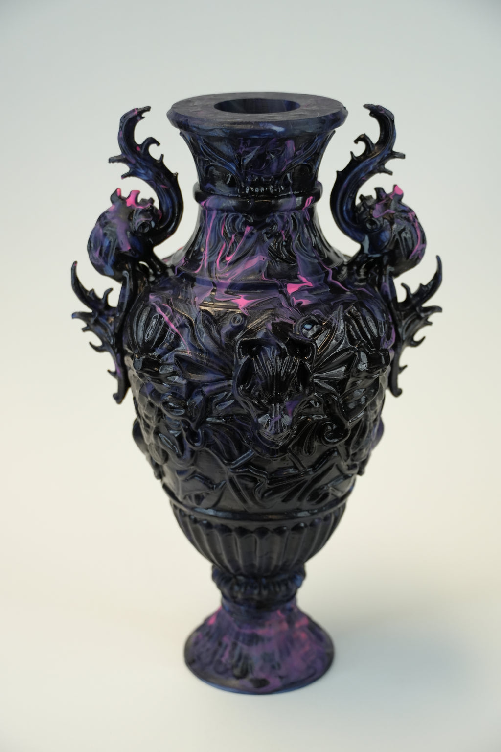 A dark purple and black ornate sculptural vase with dragon-like handles and floral relief details, photographed against a plain light background.