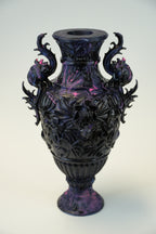 A dark purple and black ornate sculptural vase with dragon-like handles and floral relief details, photographed against a plain light background.