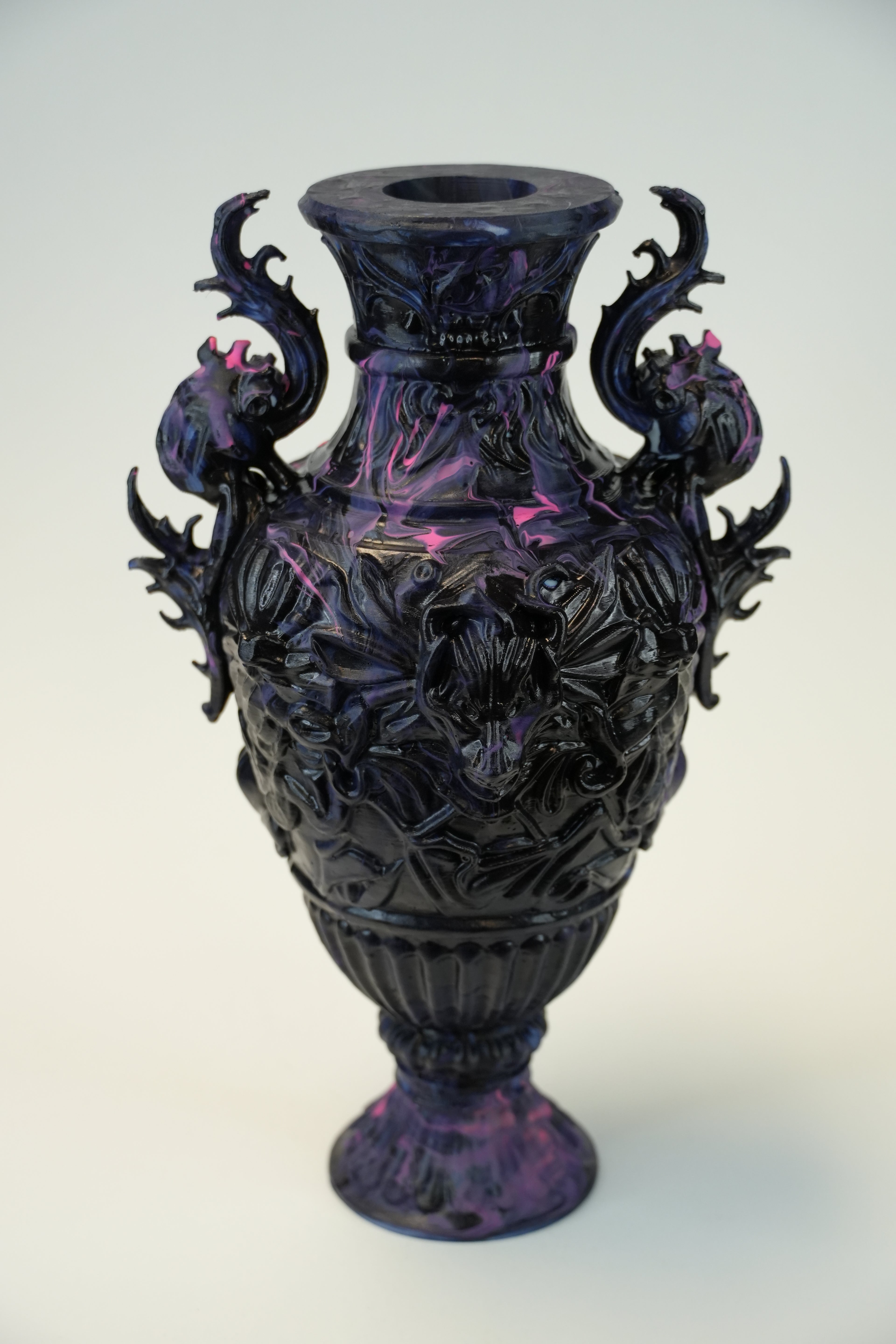 A dark purple and black ornate sculptural vase with dragon-like handles and floral relief details, photographed against a plain light background.