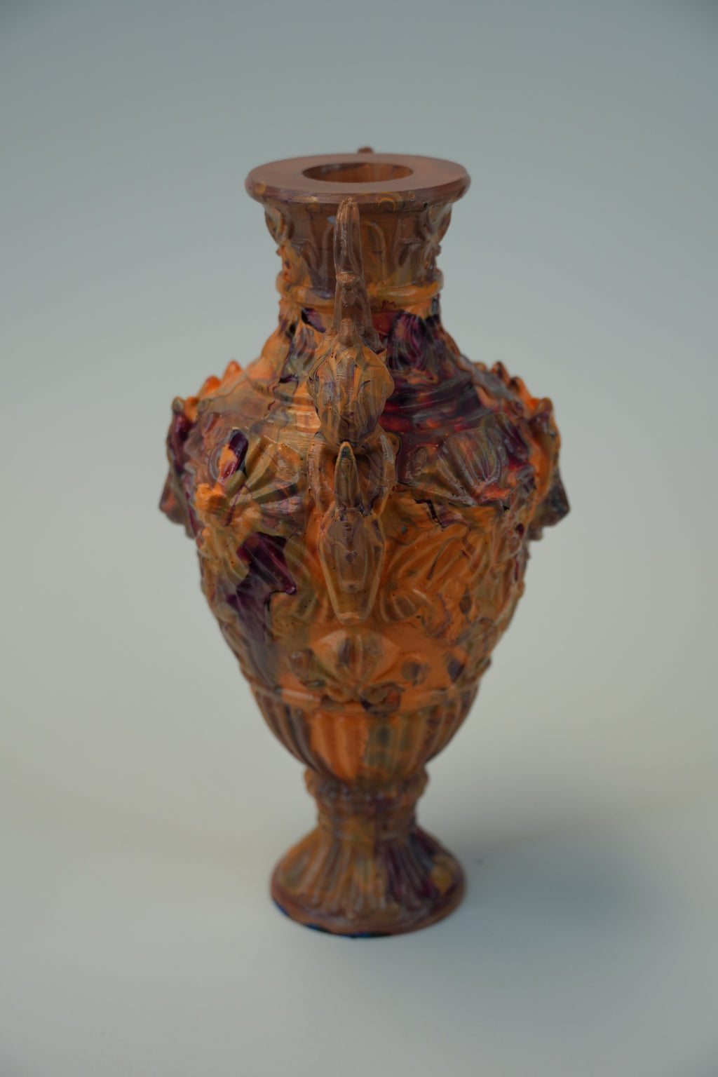 An ornate vintage-style glass vase with a bulbous body, flared neck, and pedestal base, decorated with raised floral and scroll motifs. The vase has a warm amber-brown tint with darker reddish-brown shading, photographed against a plain light gray studio background.