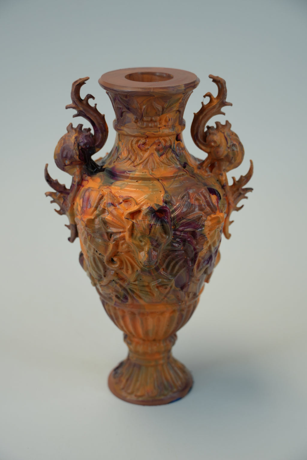 An ornate carved ceramic vase with two dragon-like handles, featuring a glossy finish with iridescent copper, gold, and purple tones, set against a plain light gray background.