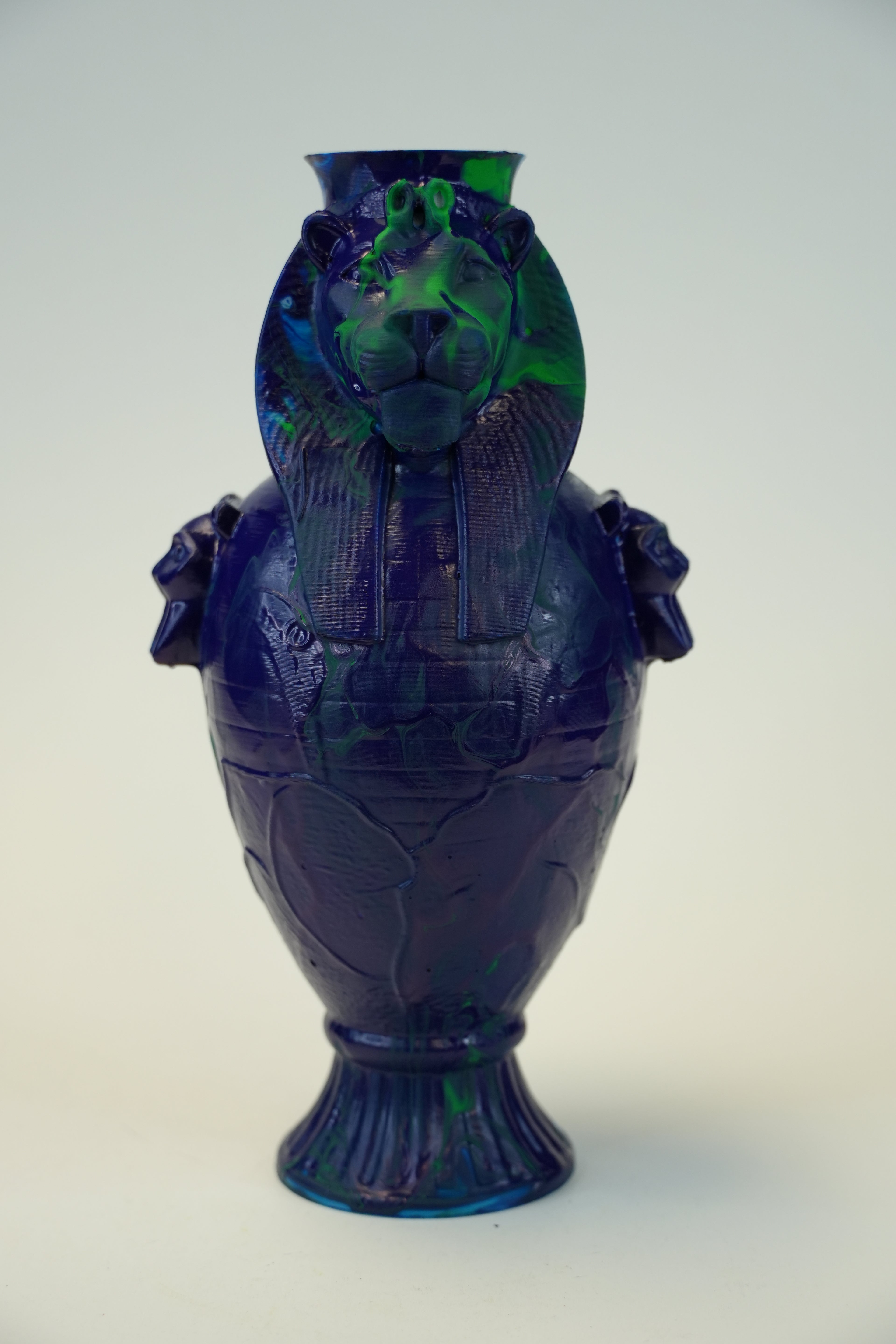 A decorative lion-shaped glass vase in deep cobalt blue with vibrant green marbled accents, shown against a plain off-white background.