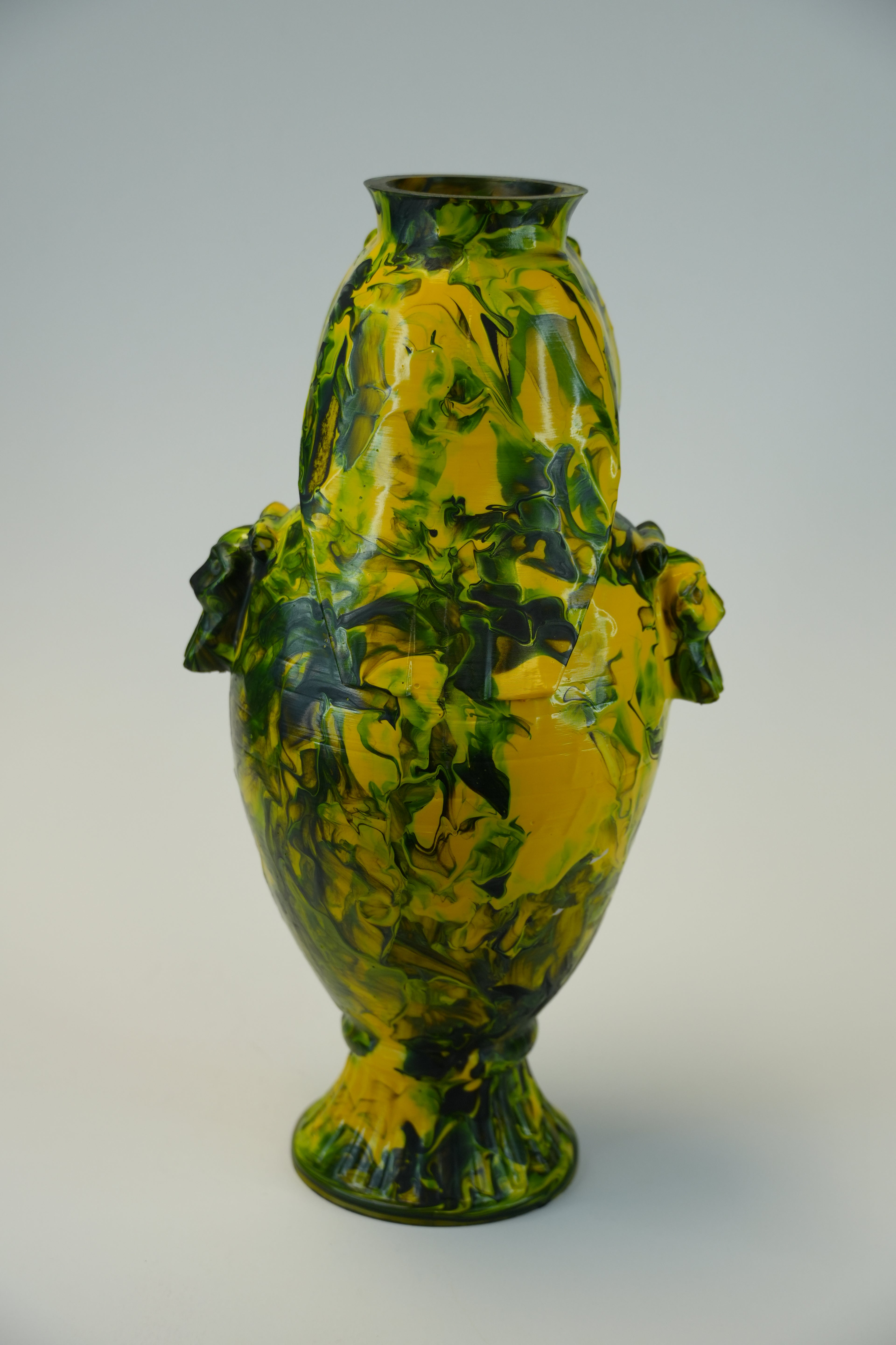 A glossy ceramic vase with a marbled pattern of yellow and dark green glaze, photographed against a plain light gray background.