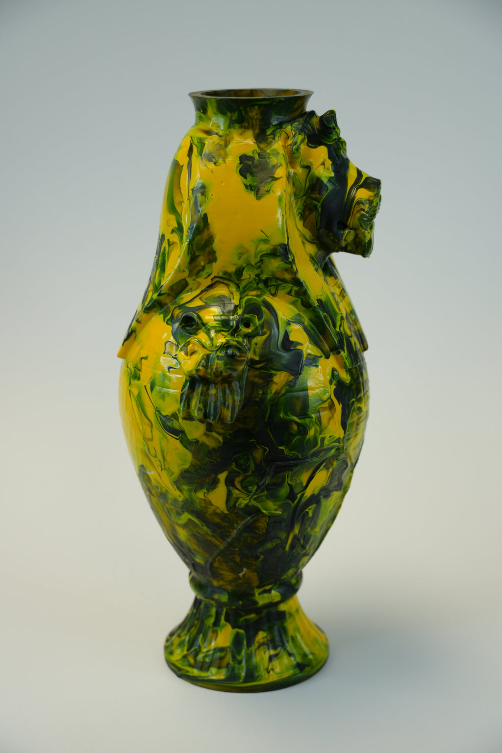 A sculptural lion-shaped ceramic vase with a glossy yellow and dark green marbled pattern, mounted on a plain light gray wall.