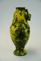 A sculptural lion-shaped ceramic vase with a glossy yellow and dark green marbled pattern, mounted on a plain light gray wall.