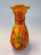 A sculptural vase shaped like a horse head, featuring a vibrant marbled pattern of yellow, orange, and red on a light gray background.