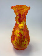 A hand-painted vase with a textured, impasto finish in yellow, orange, and red, photographed from an angle against a neutral light gray background.