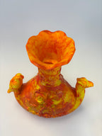 An abstract sculptural vase with a flared trumpet-like opening, featuring marbled orange, yellow, and red tones on a plain light background.