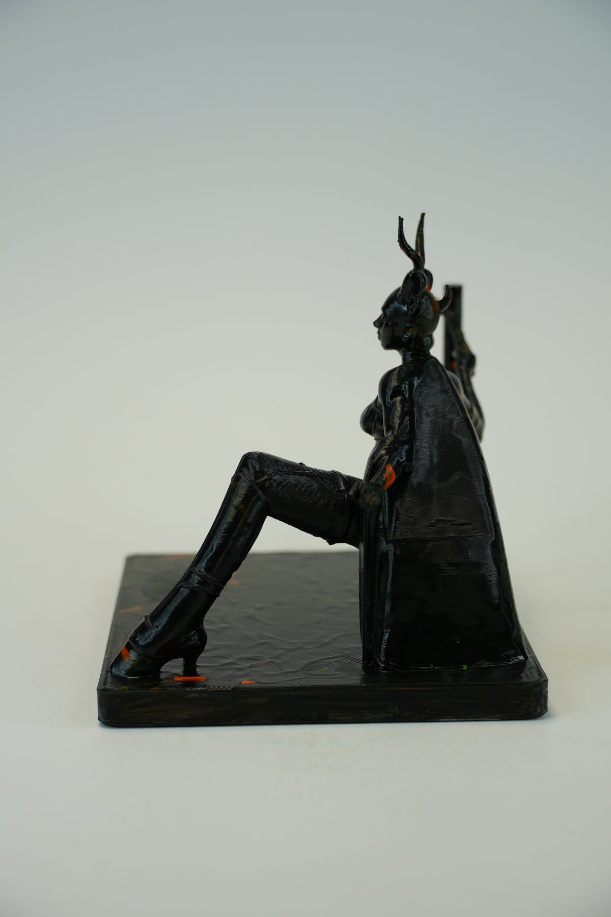 A black resin figurine of a seated female figure with antlered horns, shown from the side on a textured dark base against a light gray background.