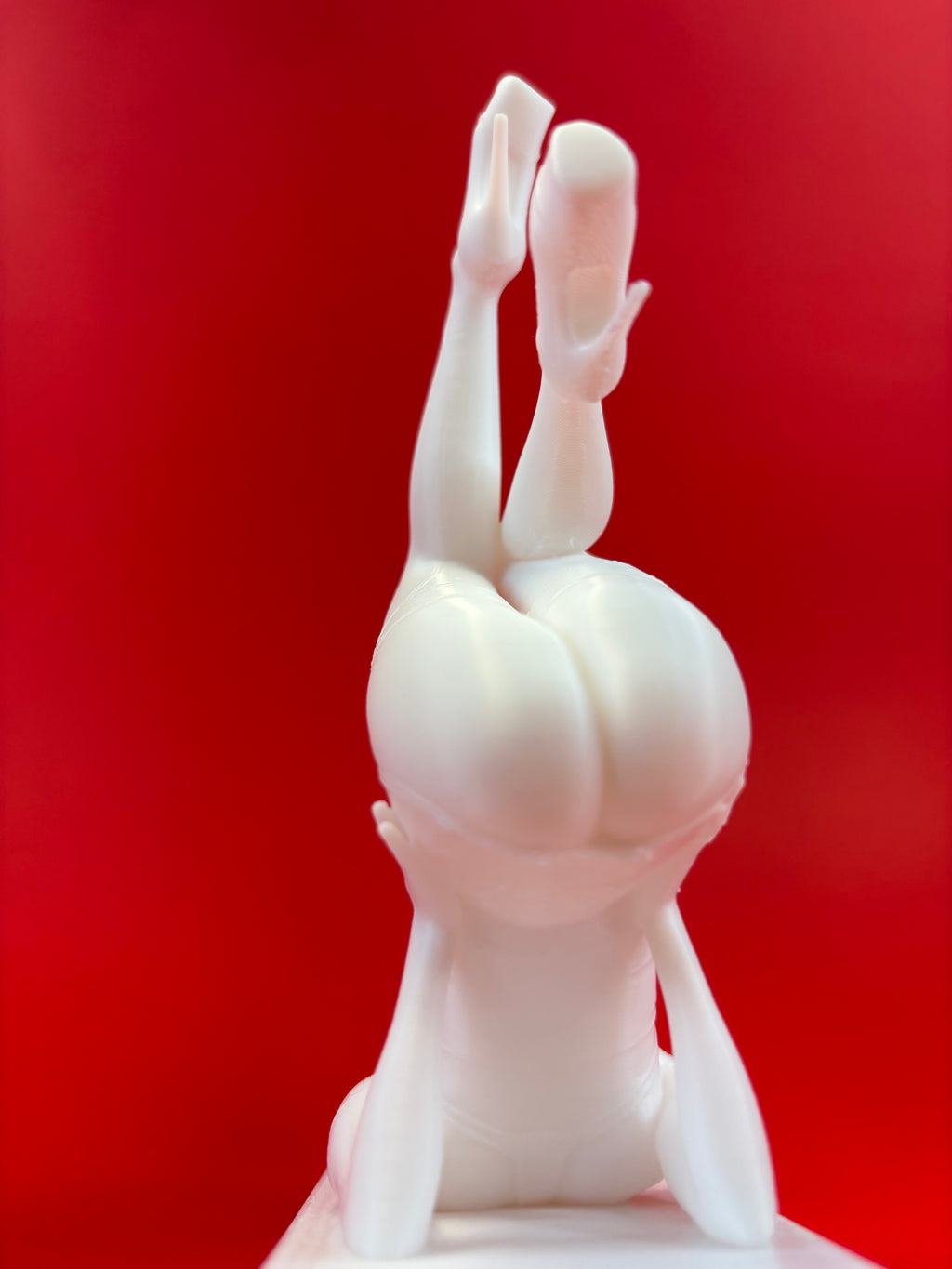 White sculpture of a figure in a headstand against a red background