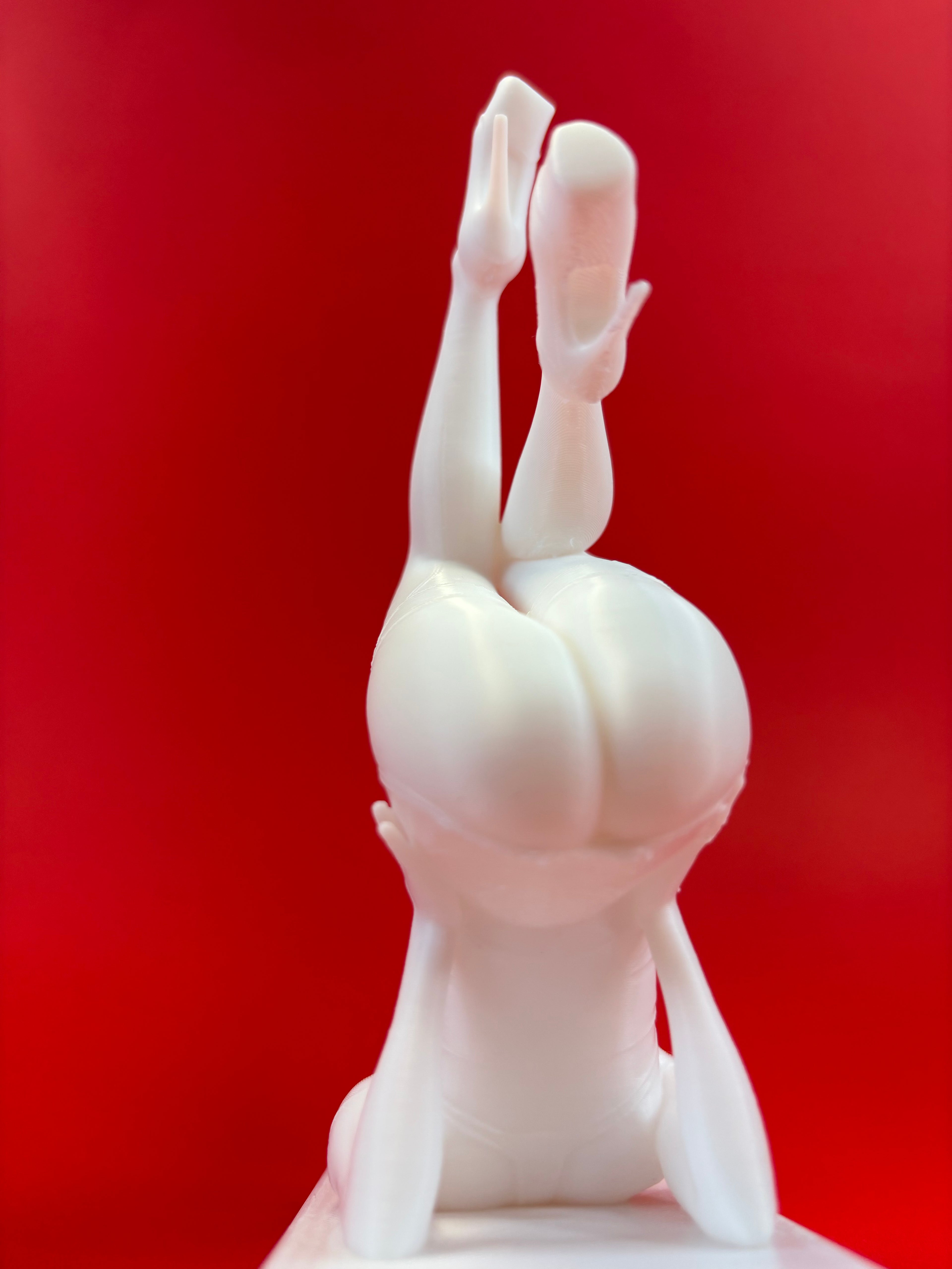 White sculpture of a figure in a headstand against a red background