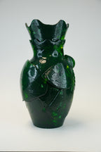 A glossy dark green glass vase with a sculptural, anatomical heart-like form and a flared, wavy rim, photographed against a neutral light gray background.