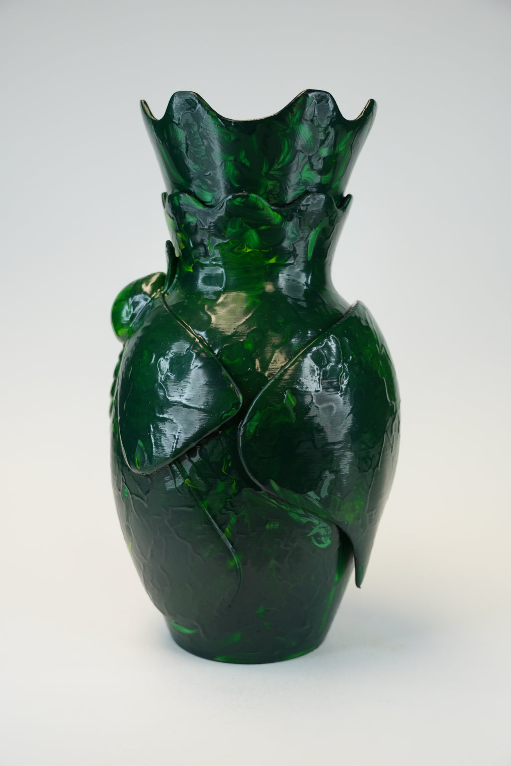 A glossy dark green glass vase with a sculptural, organic leaf-like form and a flared, scalloped rim, photographed against a clean light gray studio background.