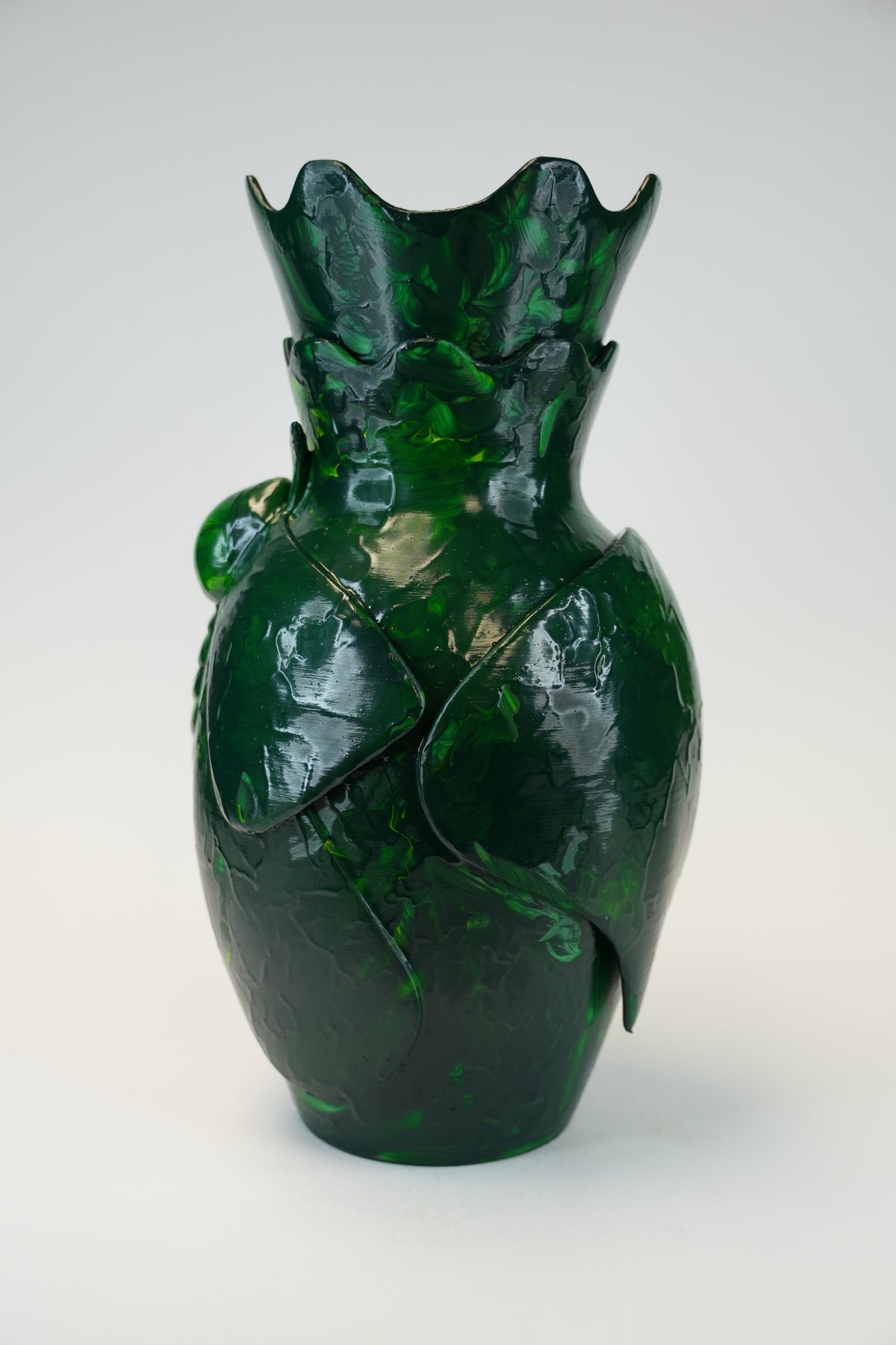 A glossy dark green glass vase with a sculptural, organic leaf-like form and a flared, scalloped rim, photographed against a clean light gray studio background.