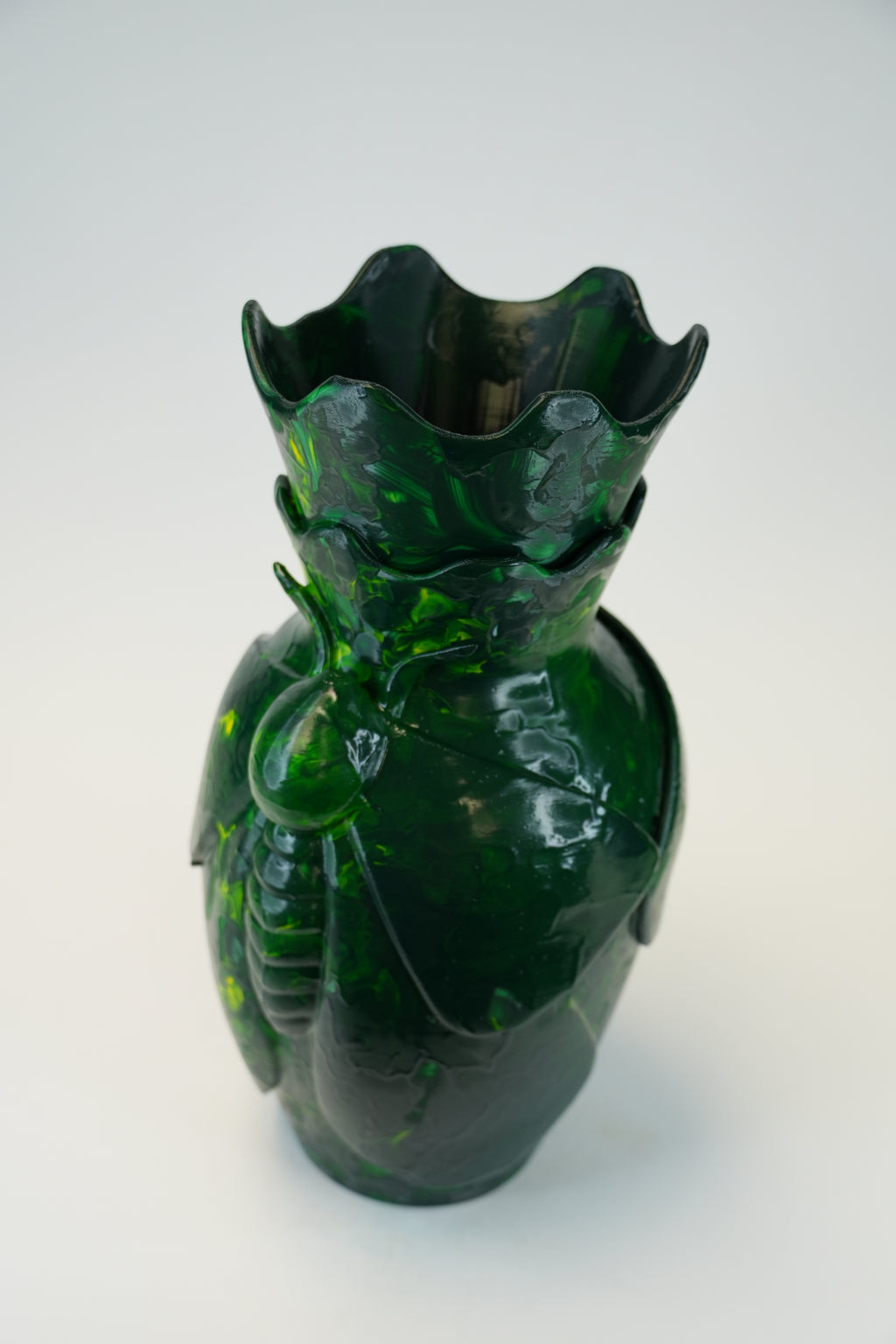 A dark green glass vase sculpted in the shape of a beetle, featuring a flared, scalloped rim and glossy highlights, set against a plain light gray background.