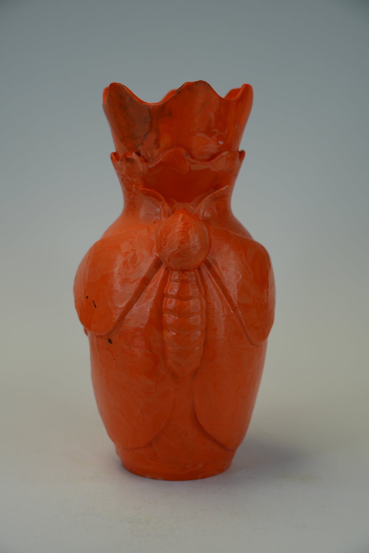 An orange-red carved ceramic vase shaped like a beetle, photographed against a neutral gray background.
