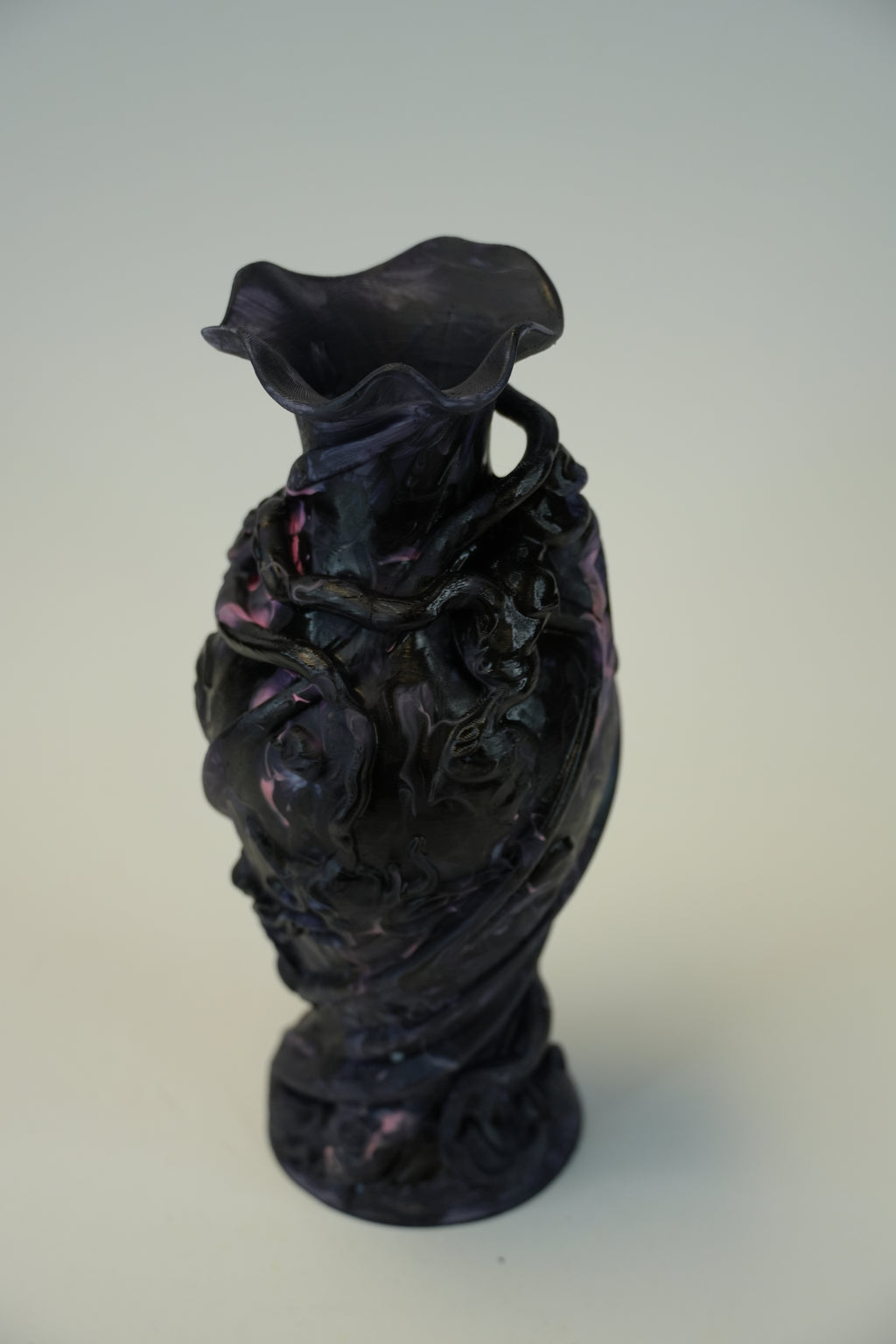 A dark, glossy sculptural vase with a flared rim and organic, face-like relief details, photographed against a plain light gray background.