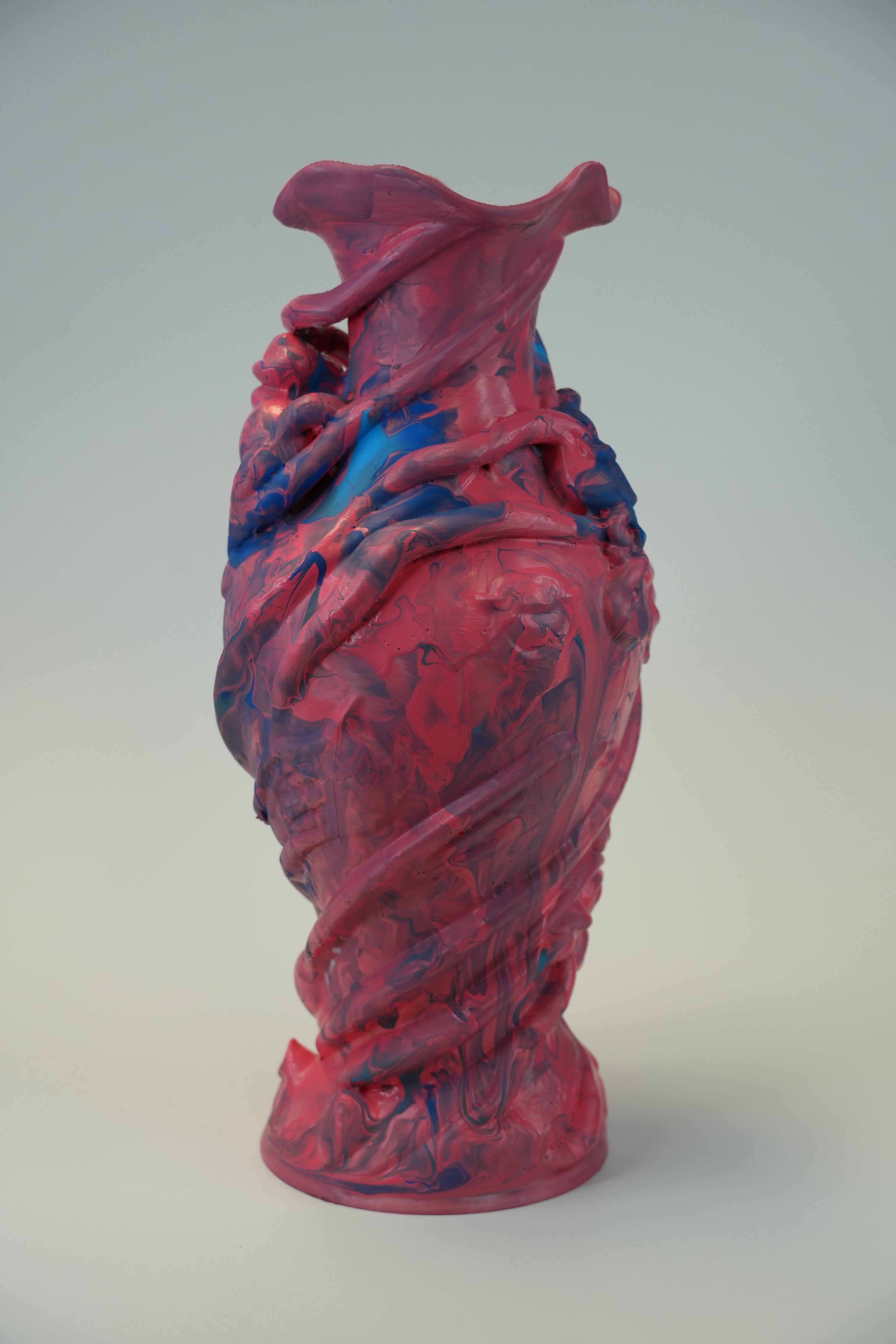 A sculptural ceramic vase with a glossy, organic, twisted form, featuring a marbled pattern of vibrant magenta pink and deep blue.
