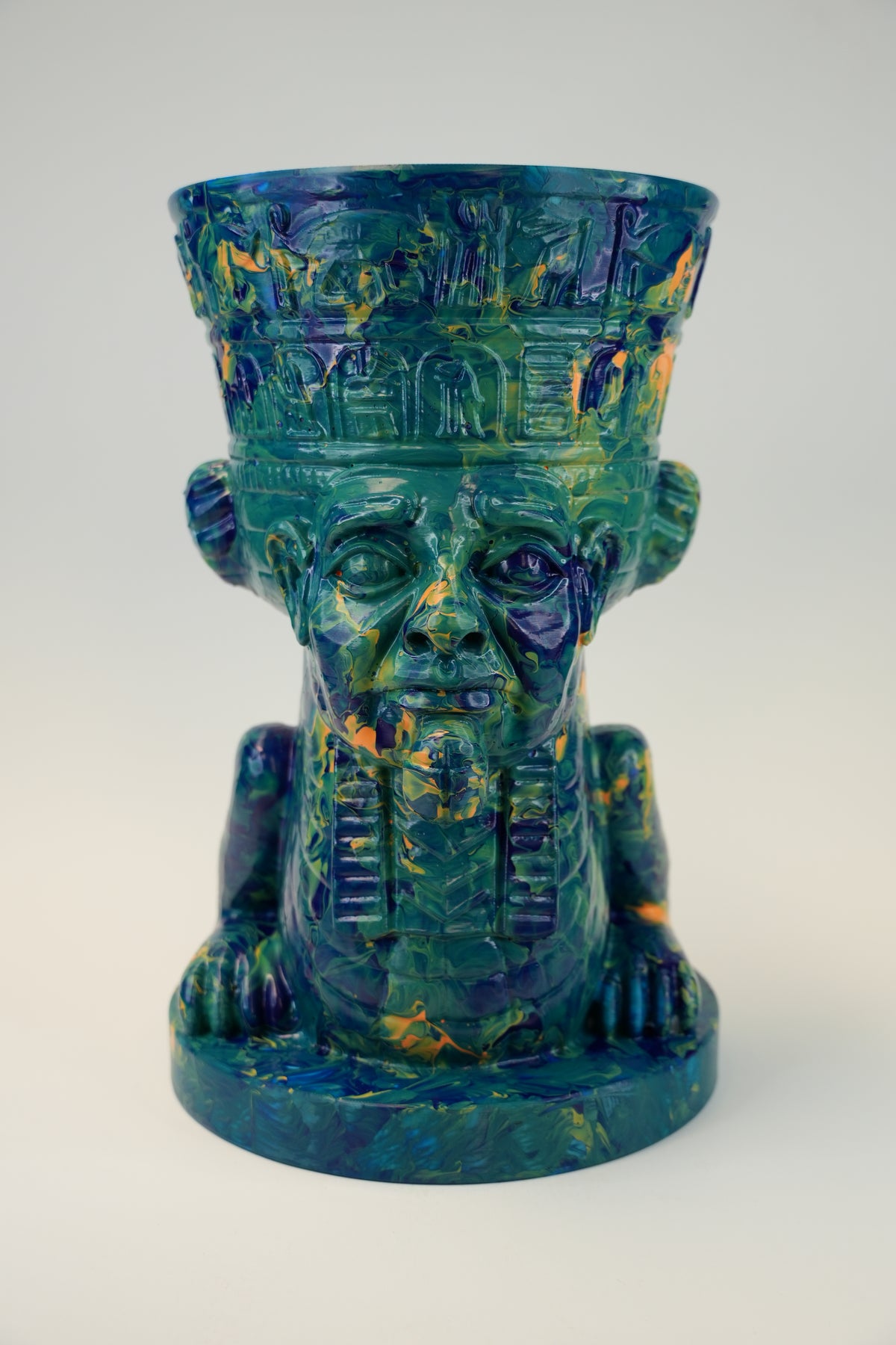 An Egyptian-style ceramic goblet or cup sculpted as a crowned pharaoh head, featuring a marbled glaze of deep teal, blue, and gold.