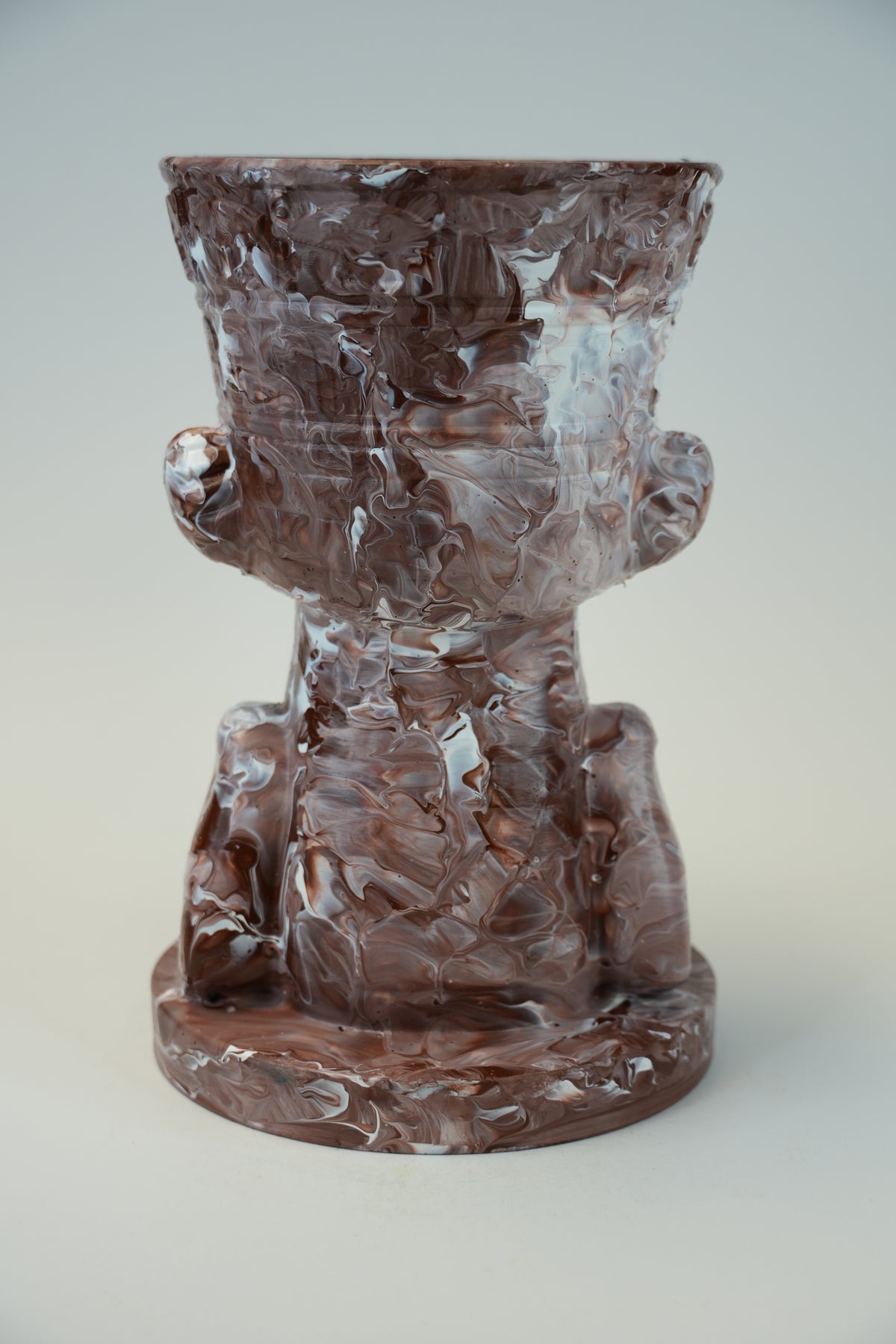 A sculptural ceramic planter shaped like a stylized seated figure, featuring a marbled terracotta and white glaze finish, set against a neutral light gray background.