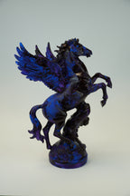 A glossy dark blue and black winged horse sculpture mounted on a plain light gray wall.