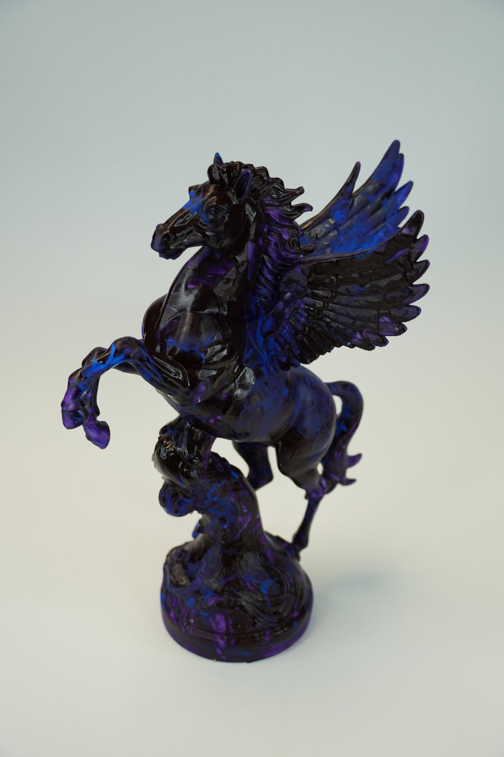 A glossy black and deep blue winged horse figurine, resembling Pegasus, standing on a textured base against a light gray background.