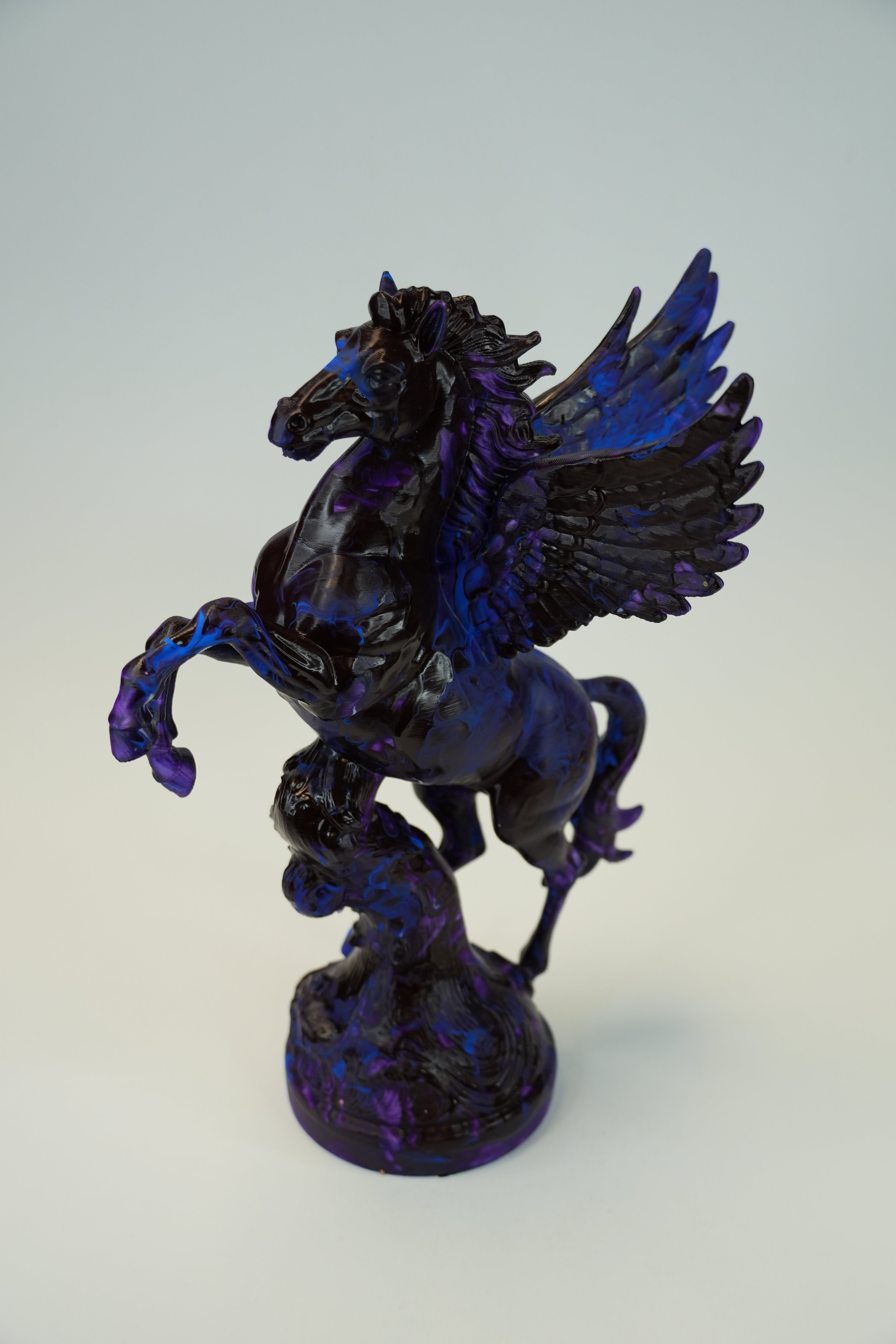 A glossy black and deep blue winged horse figurine, resembling Pegasus, standing on a textured base against a light gray background.