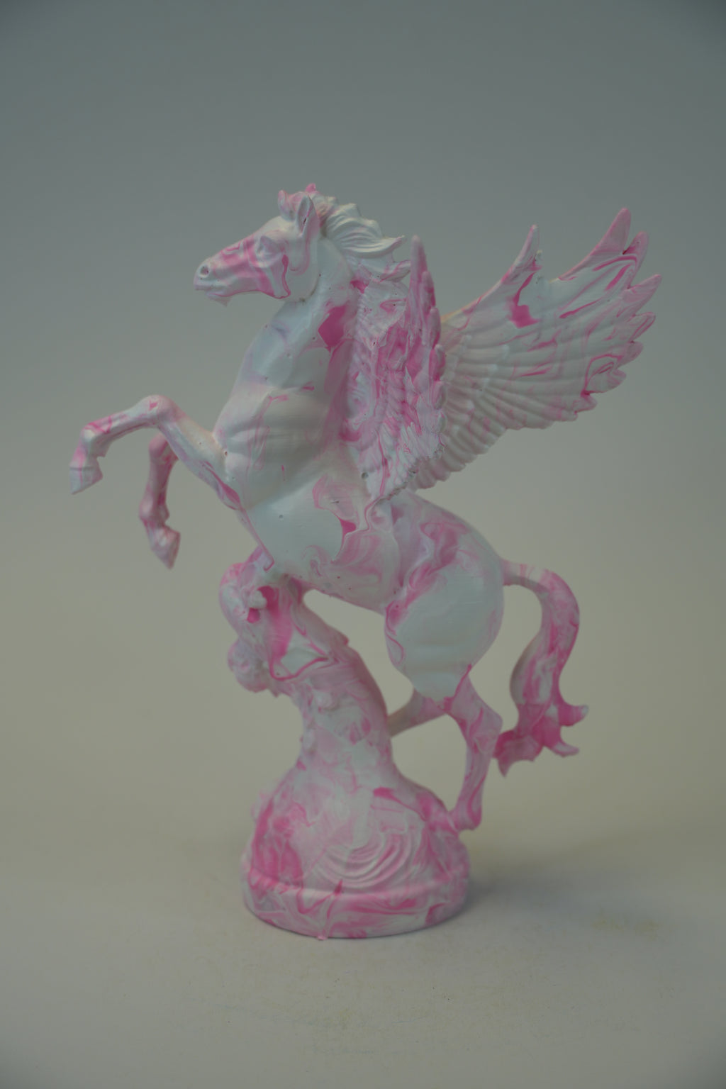 A pink and white marbled Pegasus figurine standing on a matching base, photographed against a neutral gray studio background.