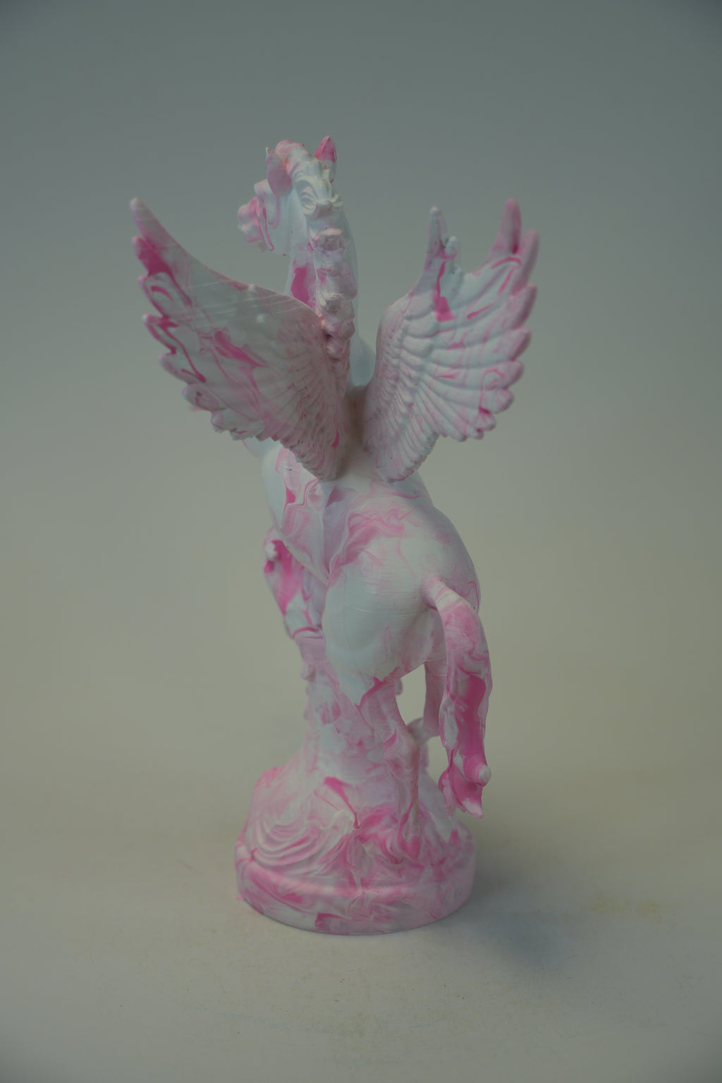A pink and white swirled pegasus figurine on a matching round base, photographed against a plain light gray background.