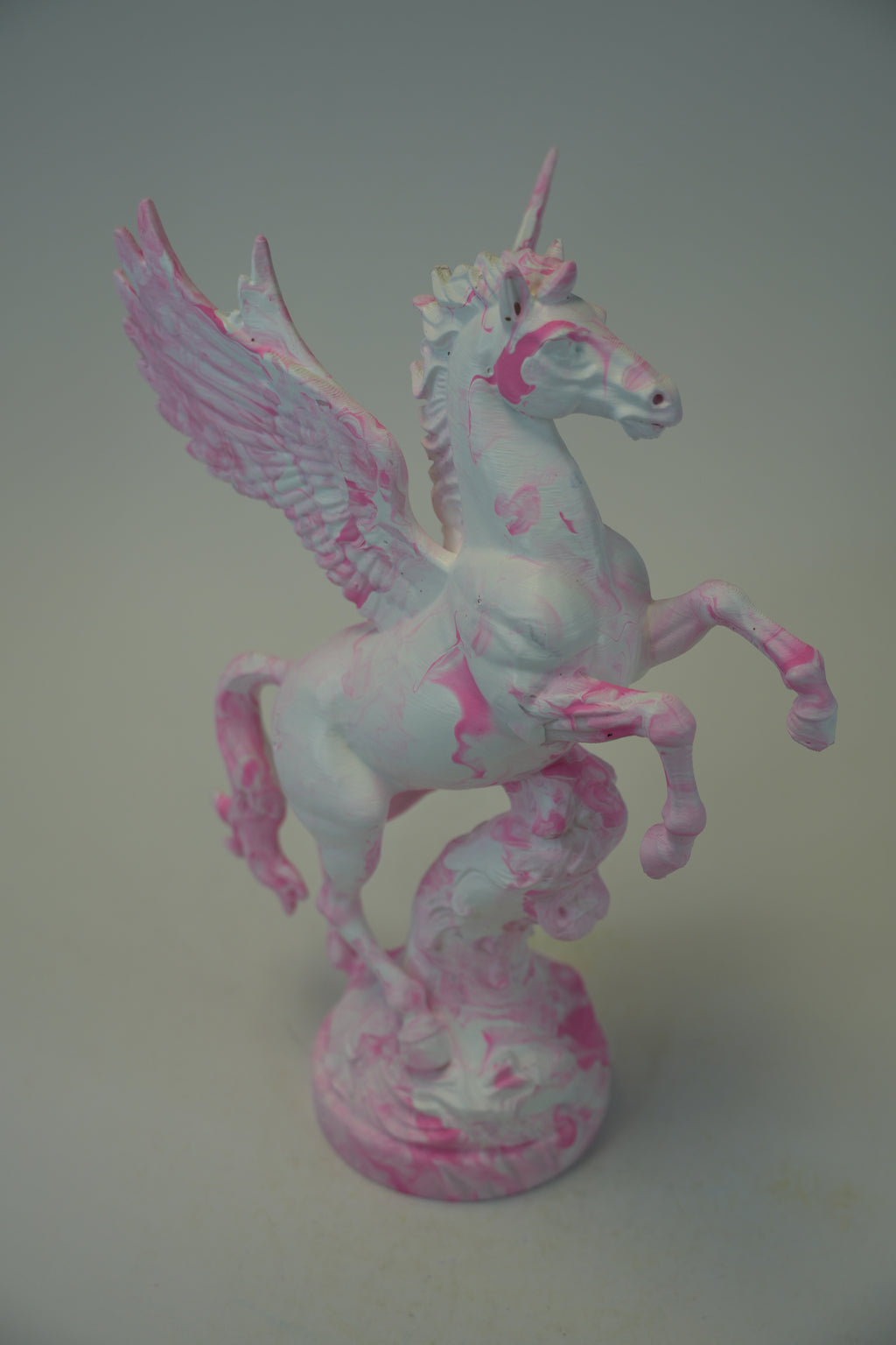 A painted Pegasus figurine with a white base and pink splatter details, standing on a matching round base against a plain gray background.