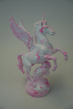 A painted Pegasus figurine with a white base and pink splatter details, standing on a matching round base against a plain gray background.