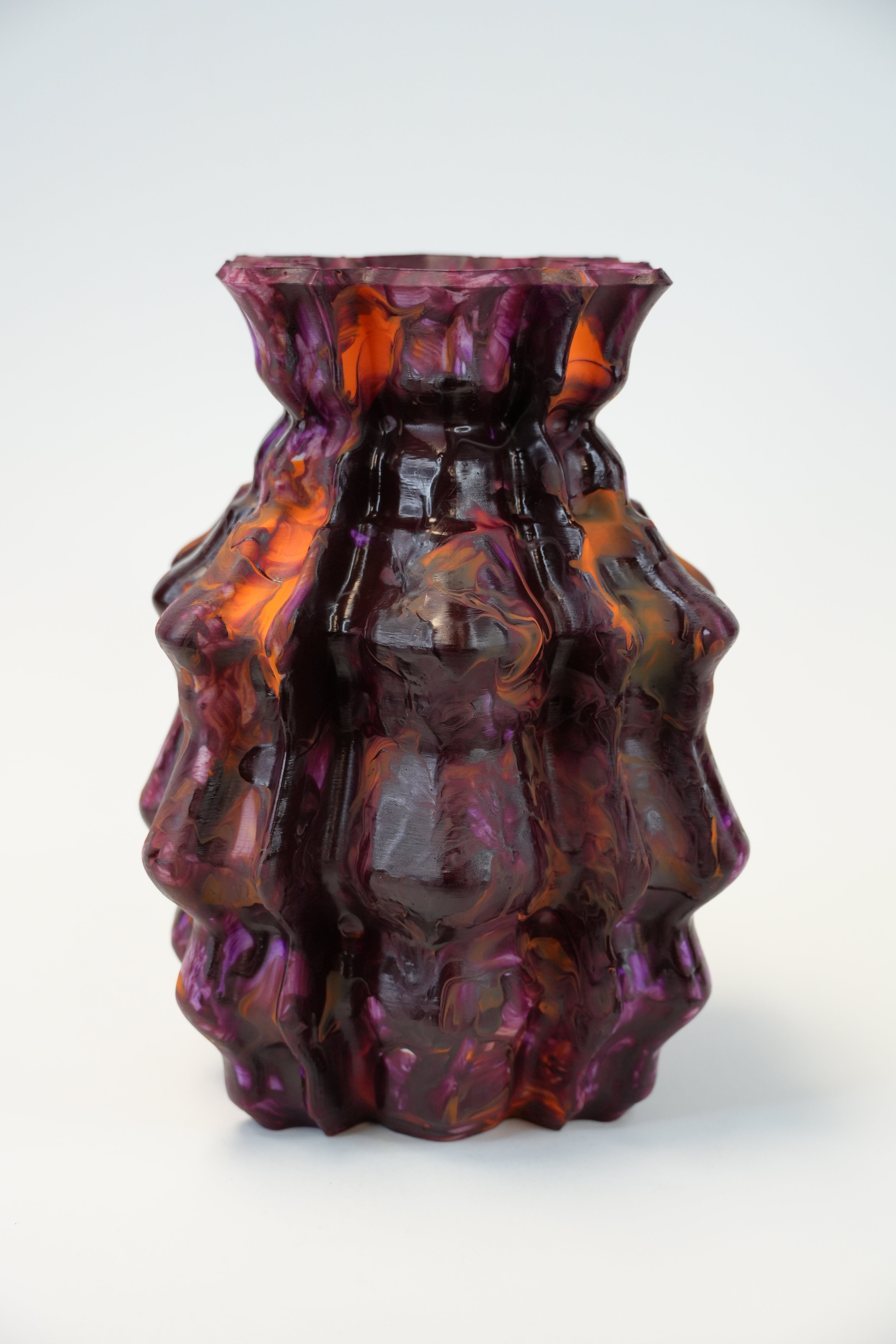 A sculptural, ribbed glass vase with a deep burgundy and amber-orange marbled pattern, photographed on a seamless white background.