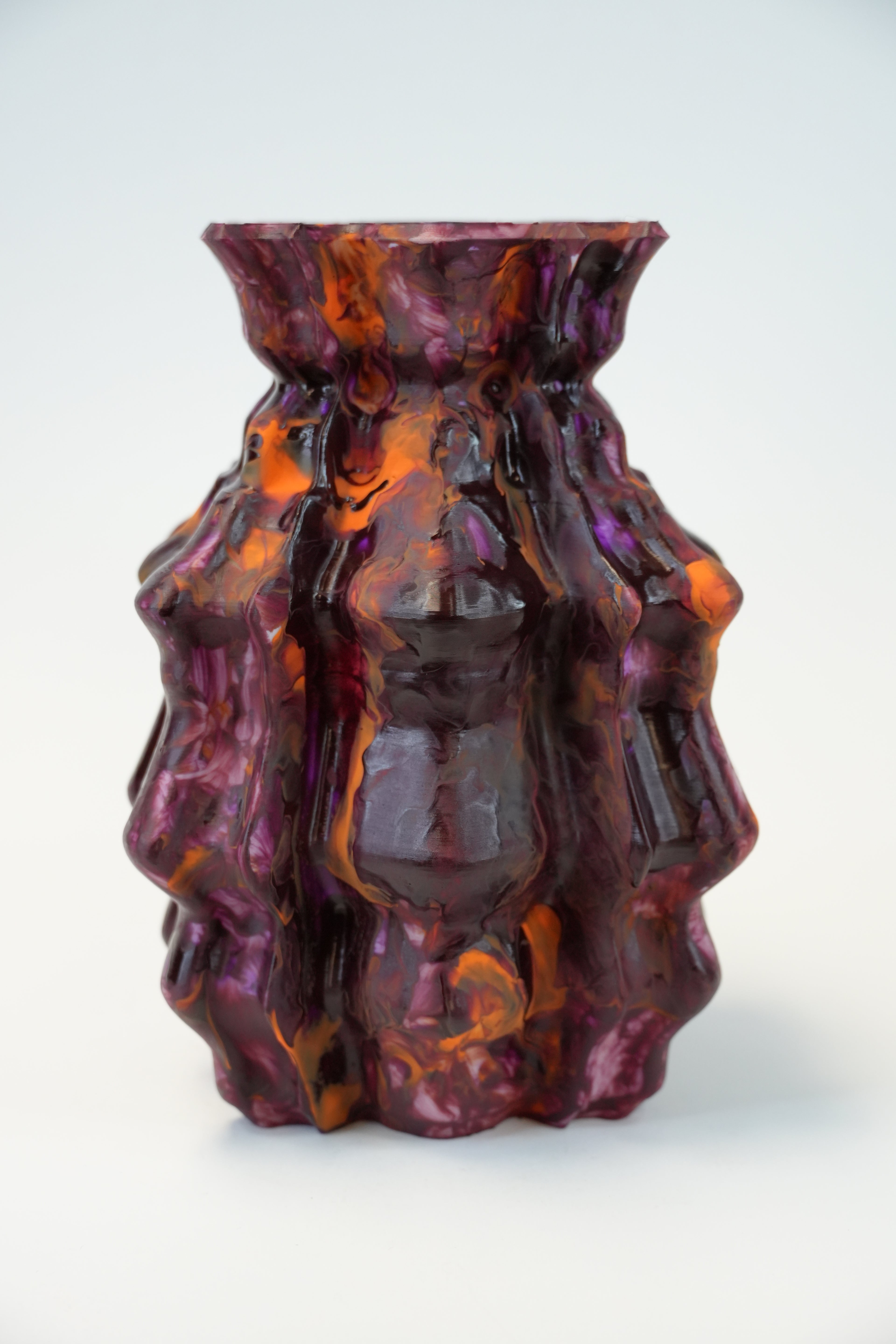 An abstract sculptural art piece made of layered, organic shapes in glossy purple, deep red, and orange, mounted on a plain white wall.