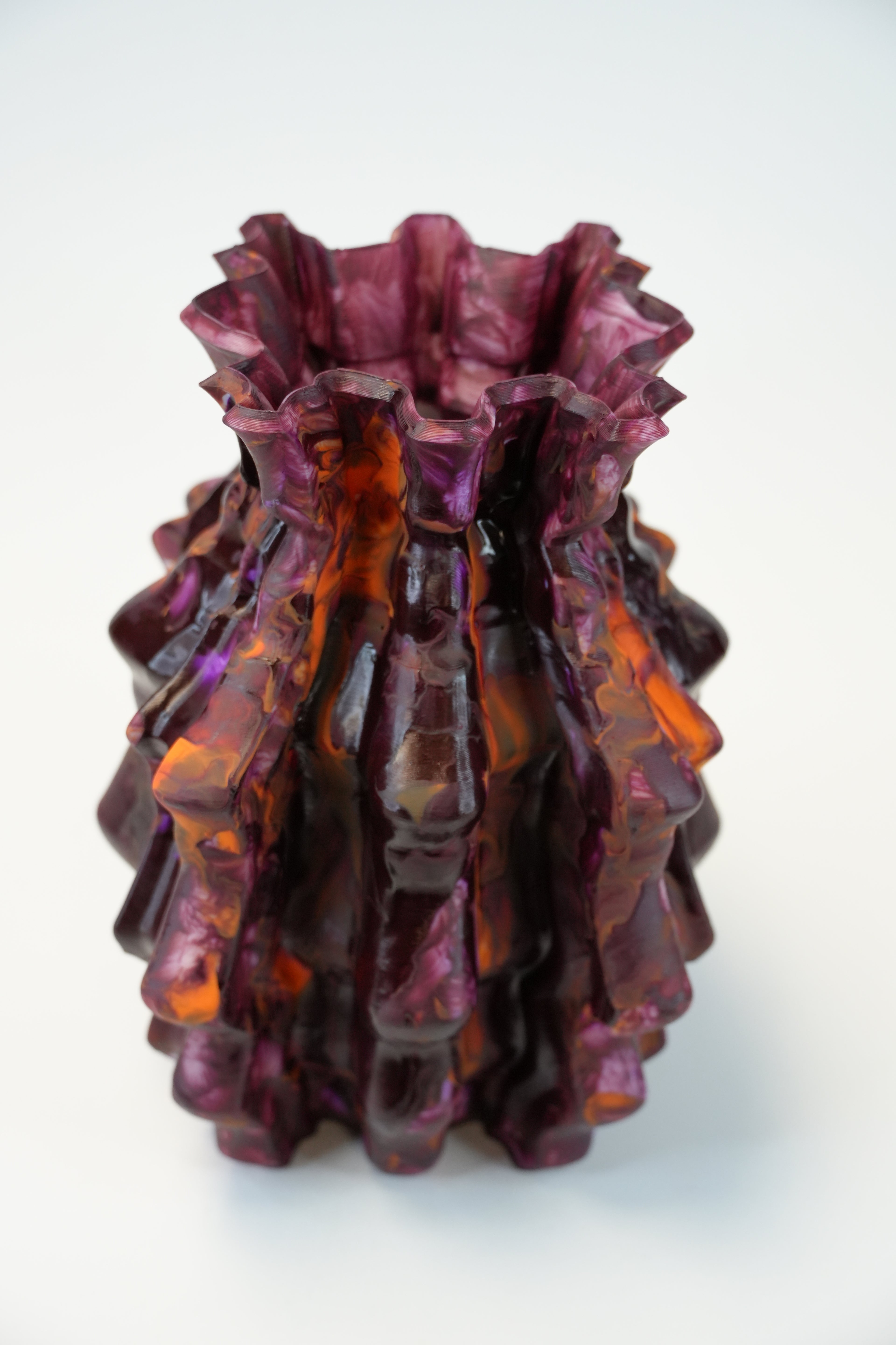 A sculptural, ruffled glass vase with a marbled pattern of deep purple, burgundy, and orange, photographed on a clean white background.